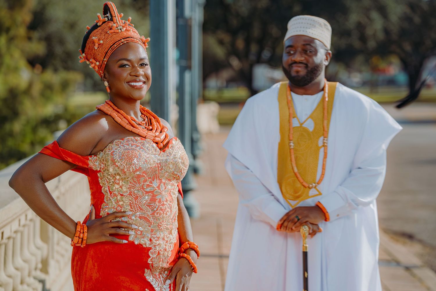 Traditional Nigerian wedding attire featuring a coral beaded dress and white agbada with gold accessories.