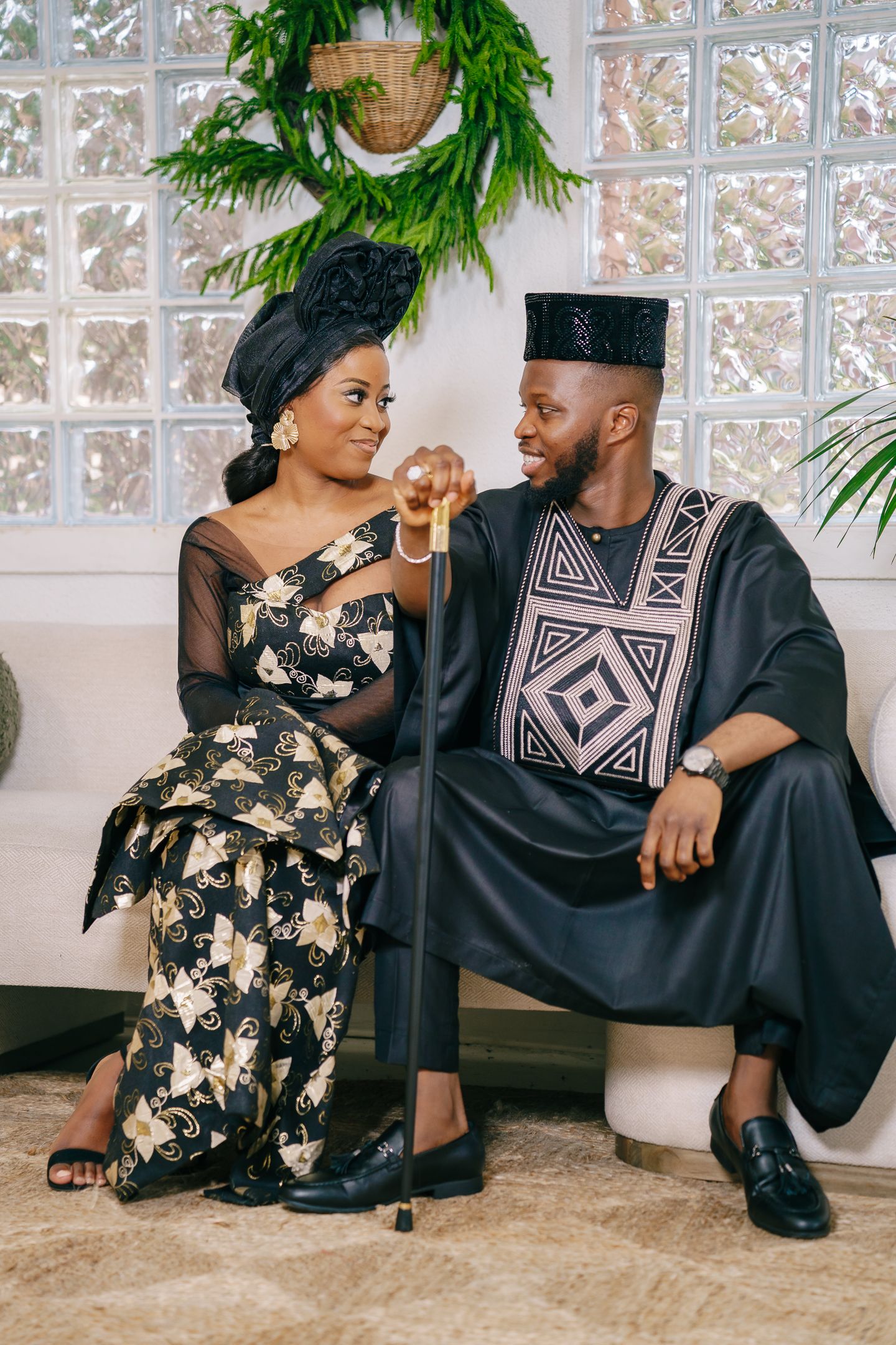 A couple in traditional Nigerian attire share intimate moments while sitting together in a bright sunlit room.