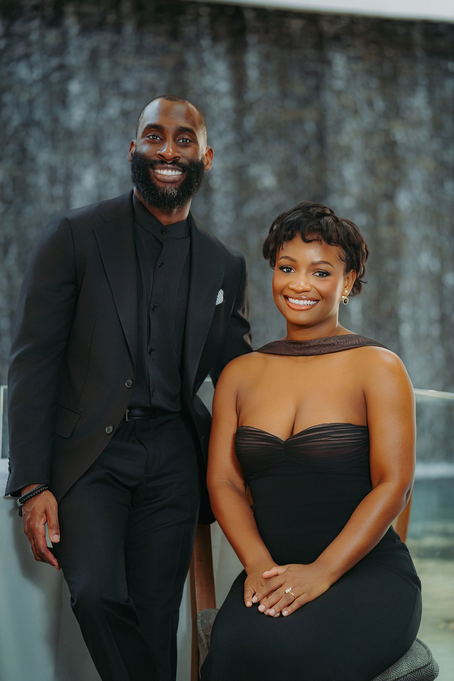 A couple poses together in coordinated black formal attire for an elegant photoshoot.