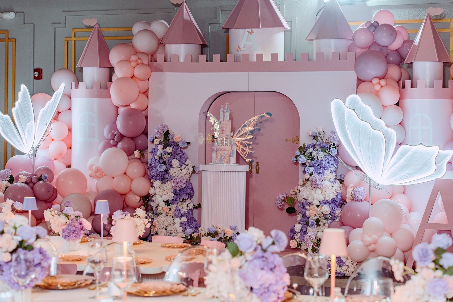 Pink castle backdrop with balloon arch decorations in pink and purple tones featuring butterfly wings and party table settings.