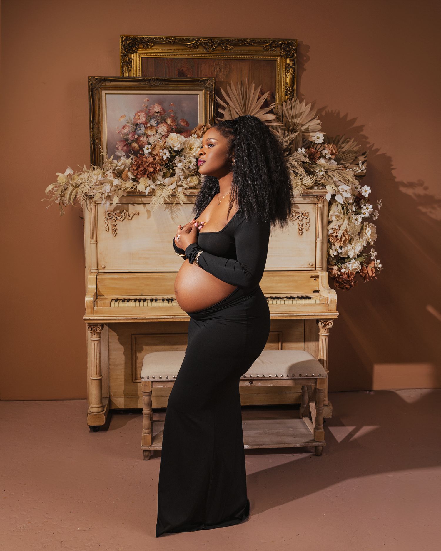 A singer in a black dress performs passionately in front of a vintage piano and floral arrangements in a warm-lit studio setting.
