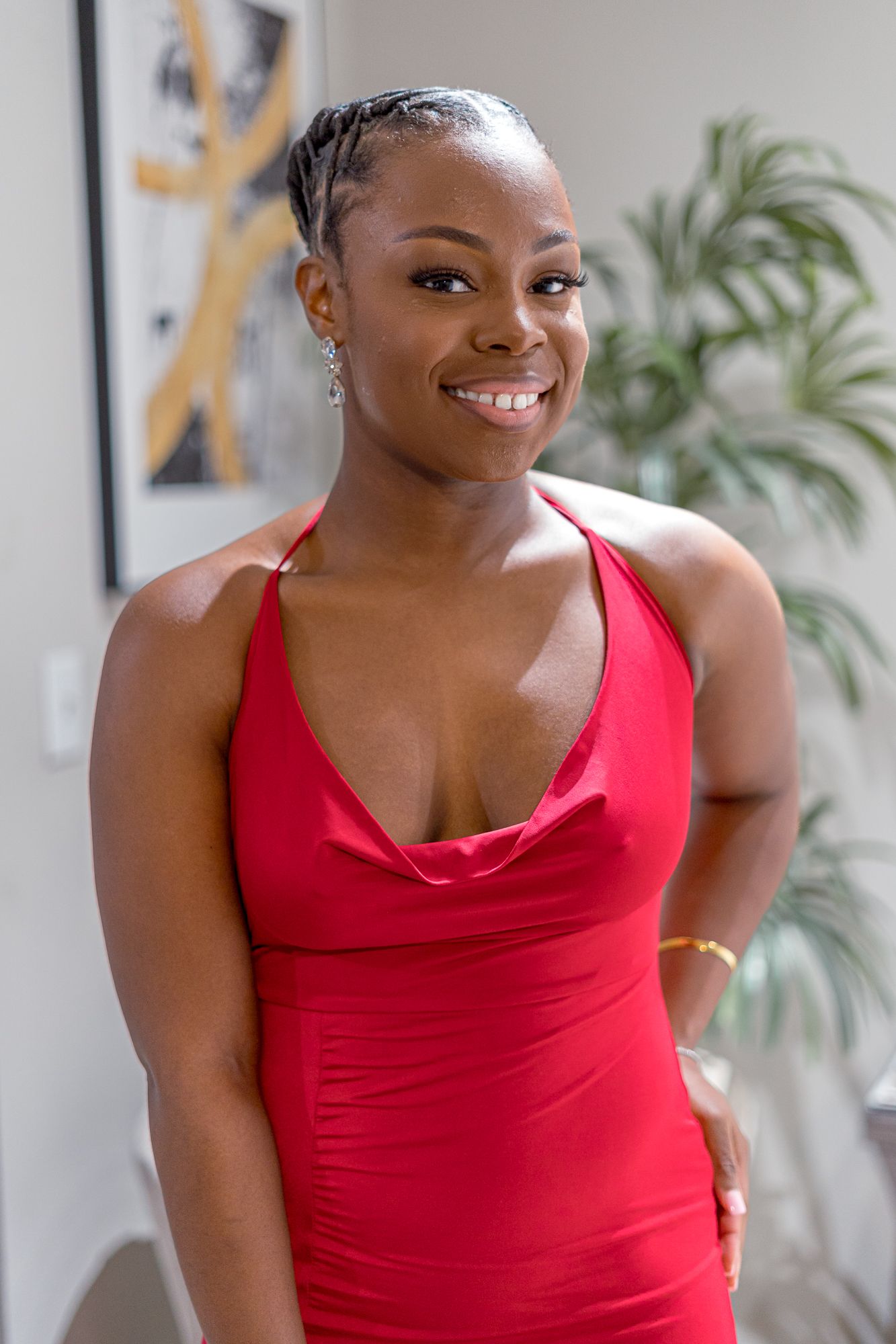 A person in a bright red sleeveless top poses against a light background with indoor plants visible.