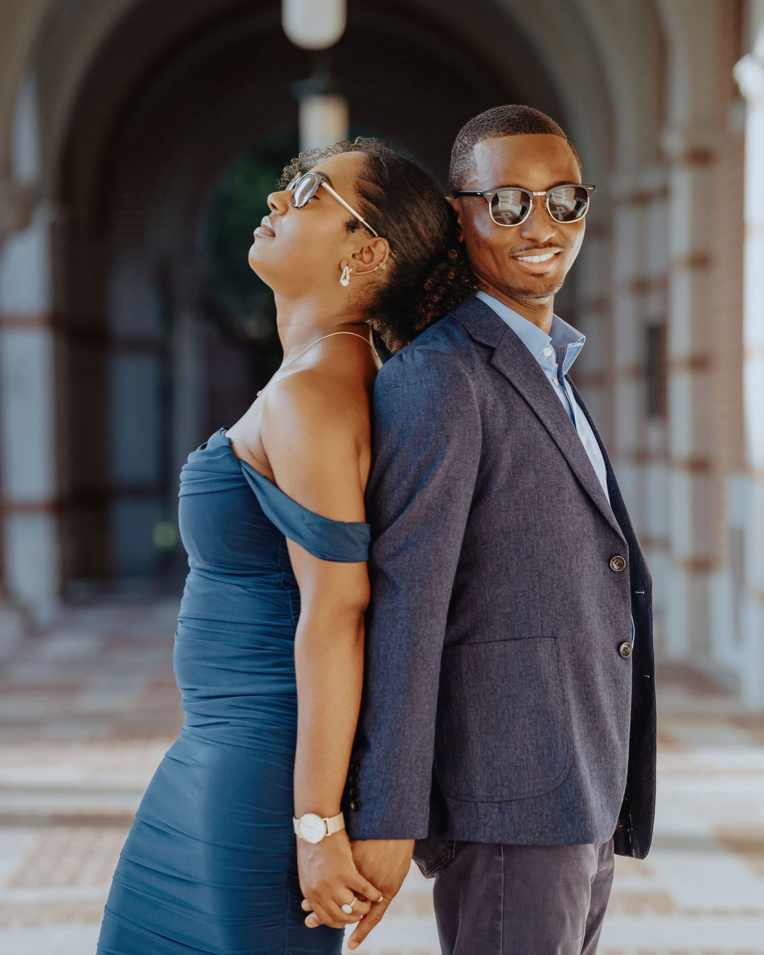 Stylish Black couple posing back-to-back in coordinating blue outfits and sunglasses in an elegant archway.