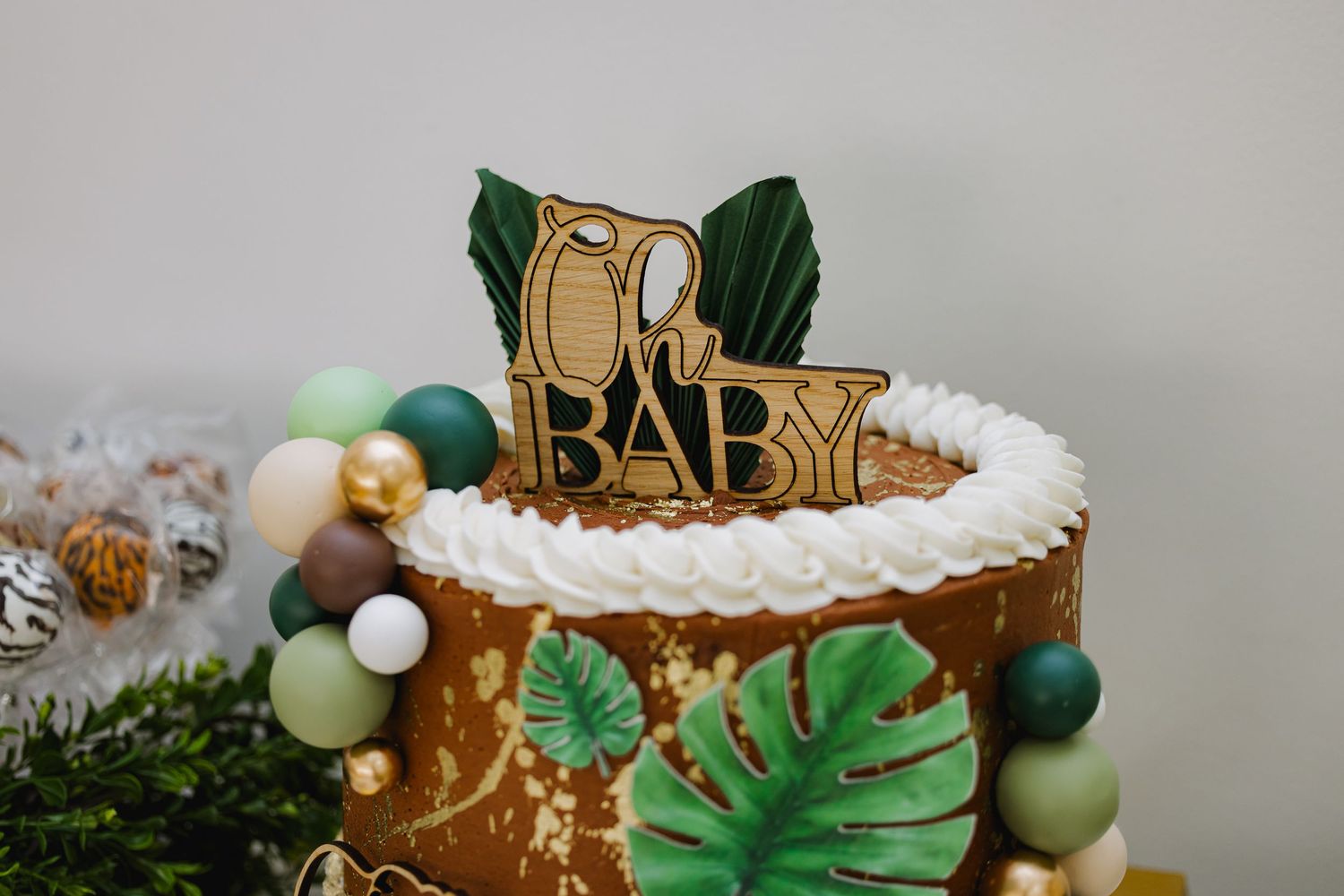 Tropical themed baby shower cake decorated with gold accents, palm leaves, and white frosting details.