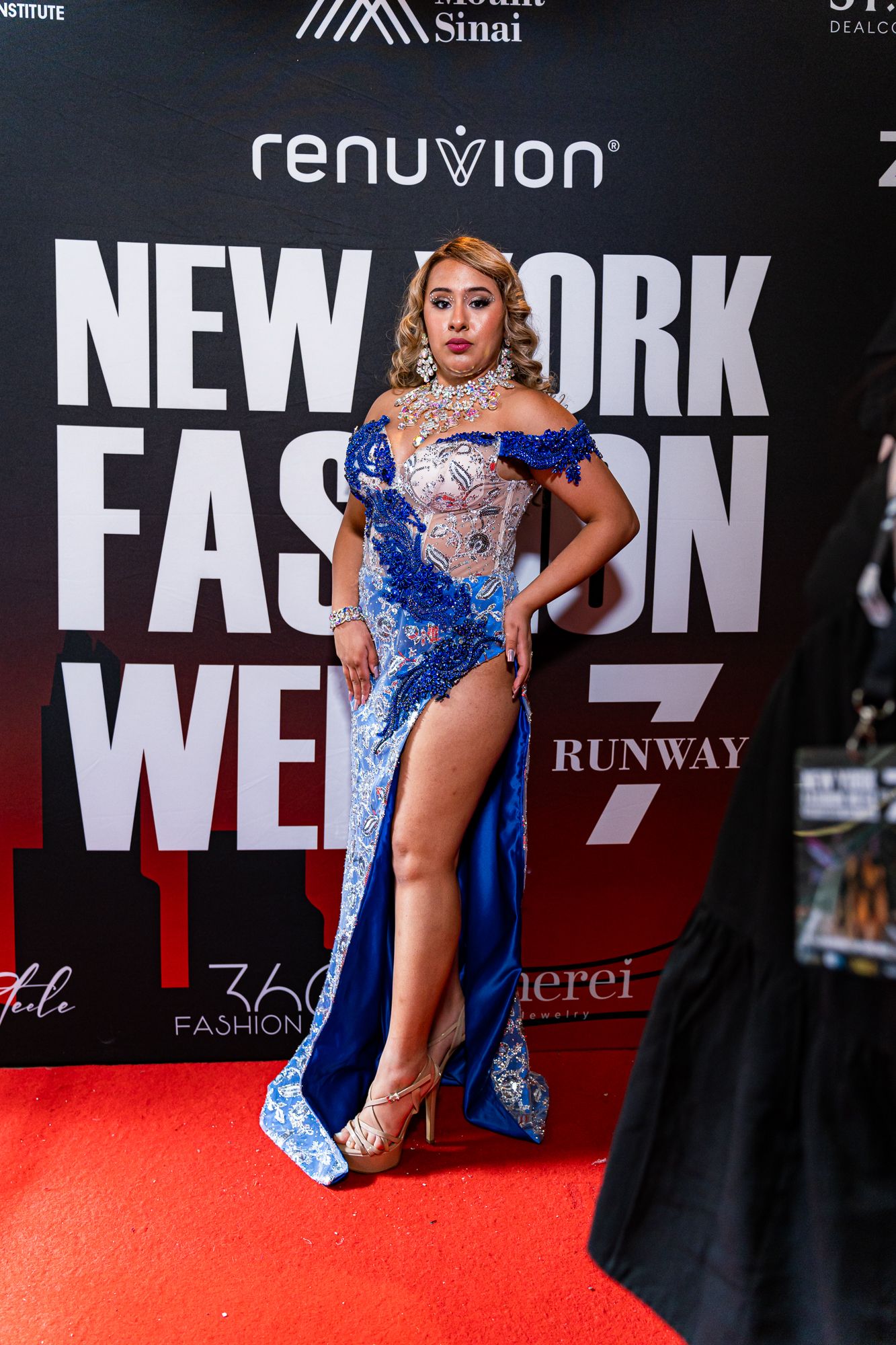 A performer in a sparkling blue dress strikes multiple poses on a red carpet at New York Fashion Week.