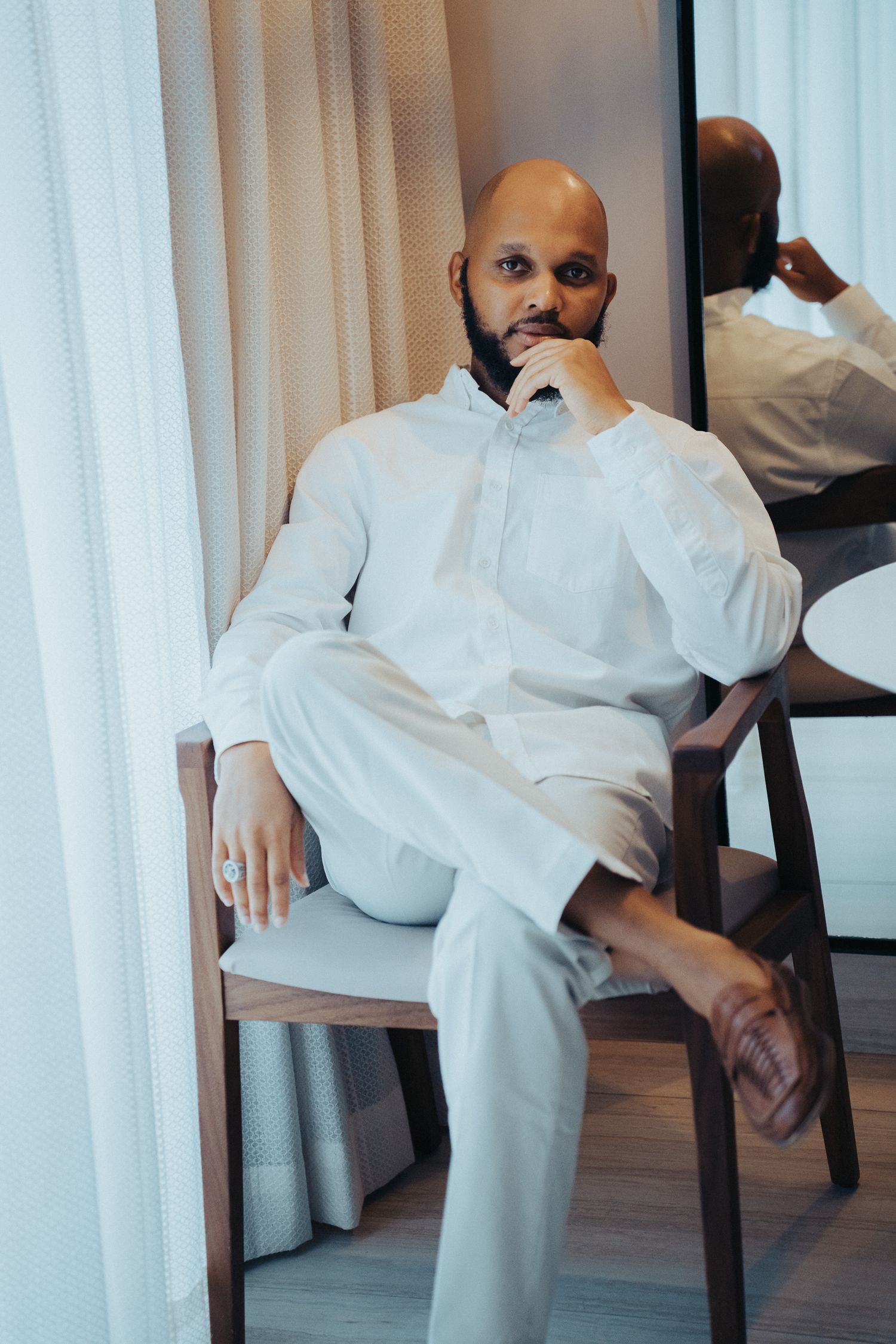 Artistic wedding photo series showing a groom in all white attire seated against white curtains.