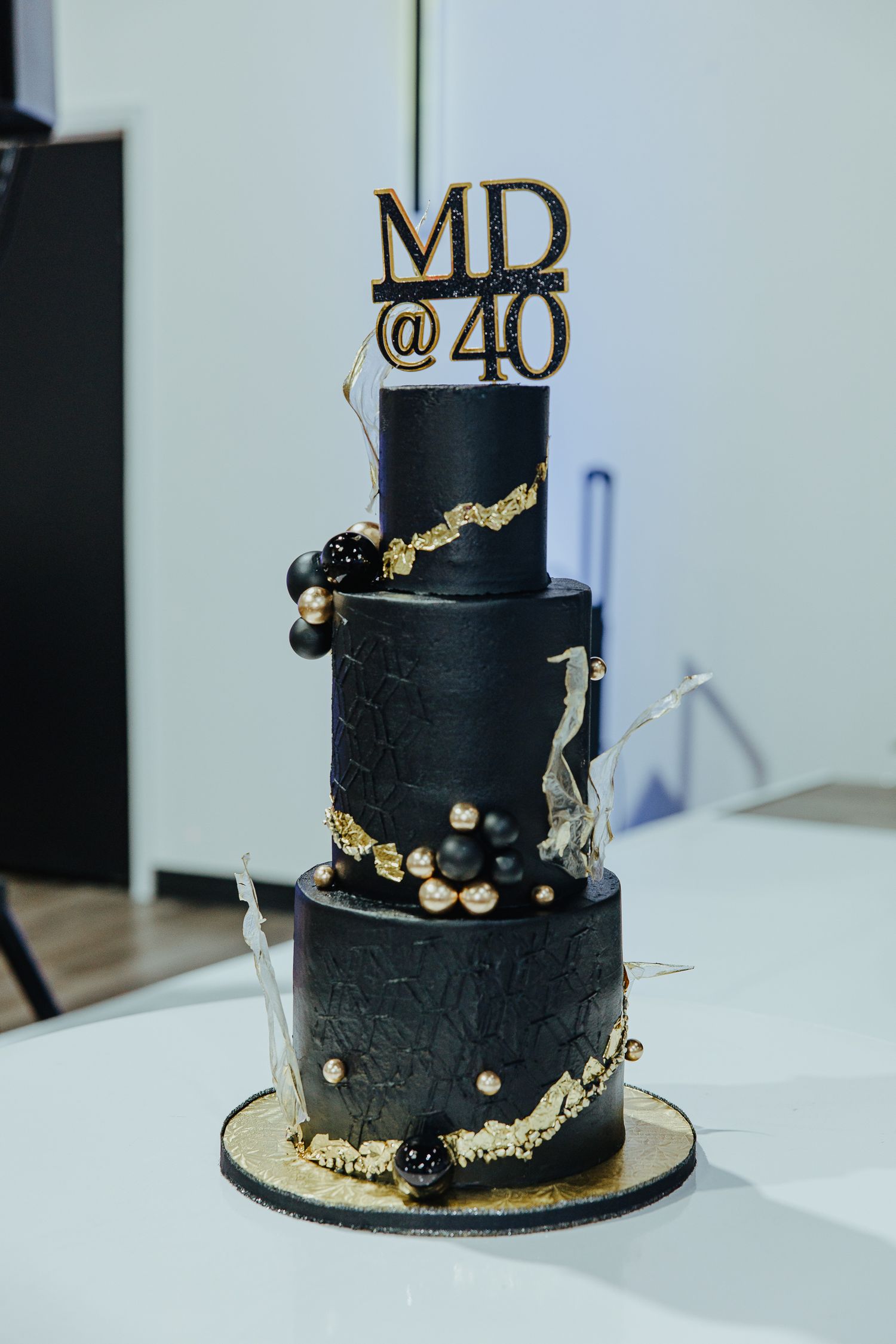 Elegant black and gold three-tier 40th birthday cake with metallic accents and intricate floral decorations.