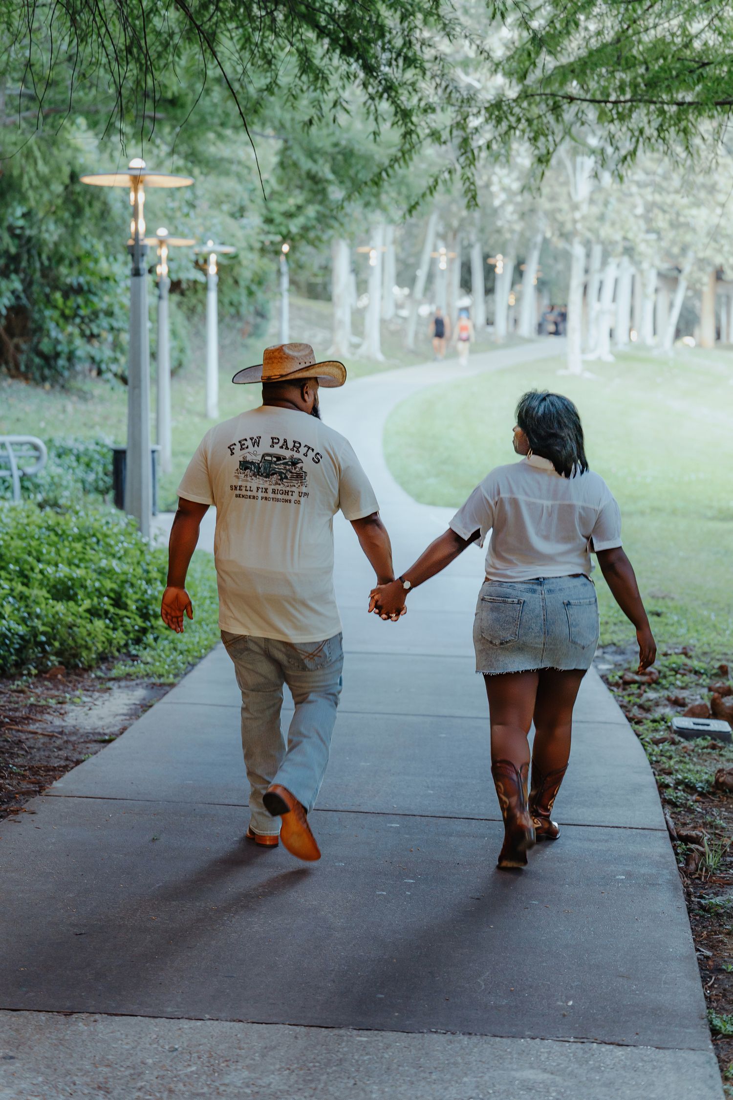 Couple walking hand in hand on park pathway wearing matching t-shirts.