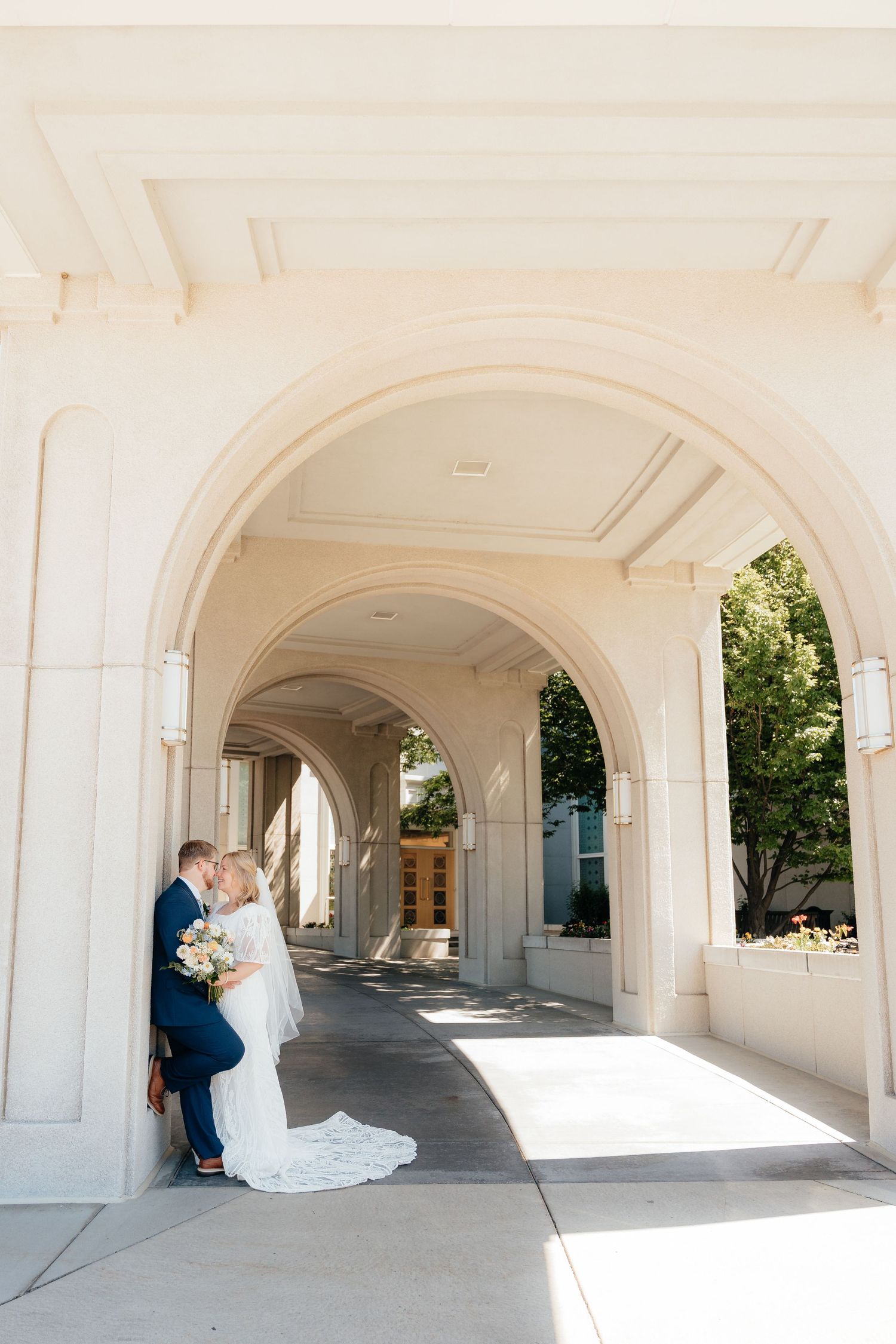 Bride and groom share a romantic kiss under elegant white arched columns of a wedding venue.