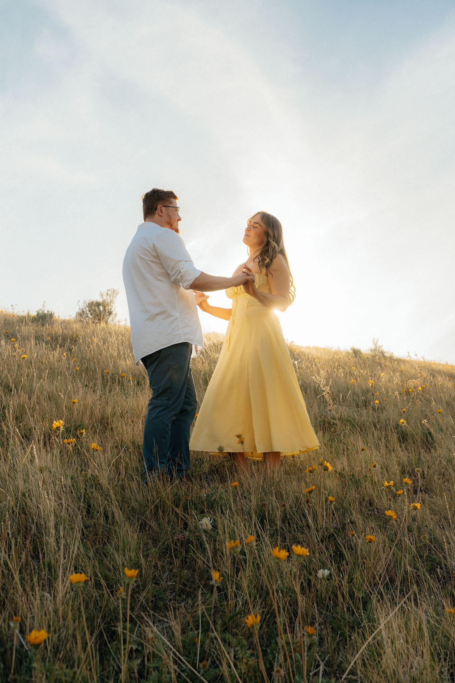 Couple dancing in a sunny field of wildflowers, woman in yellow dress, golden hour light.