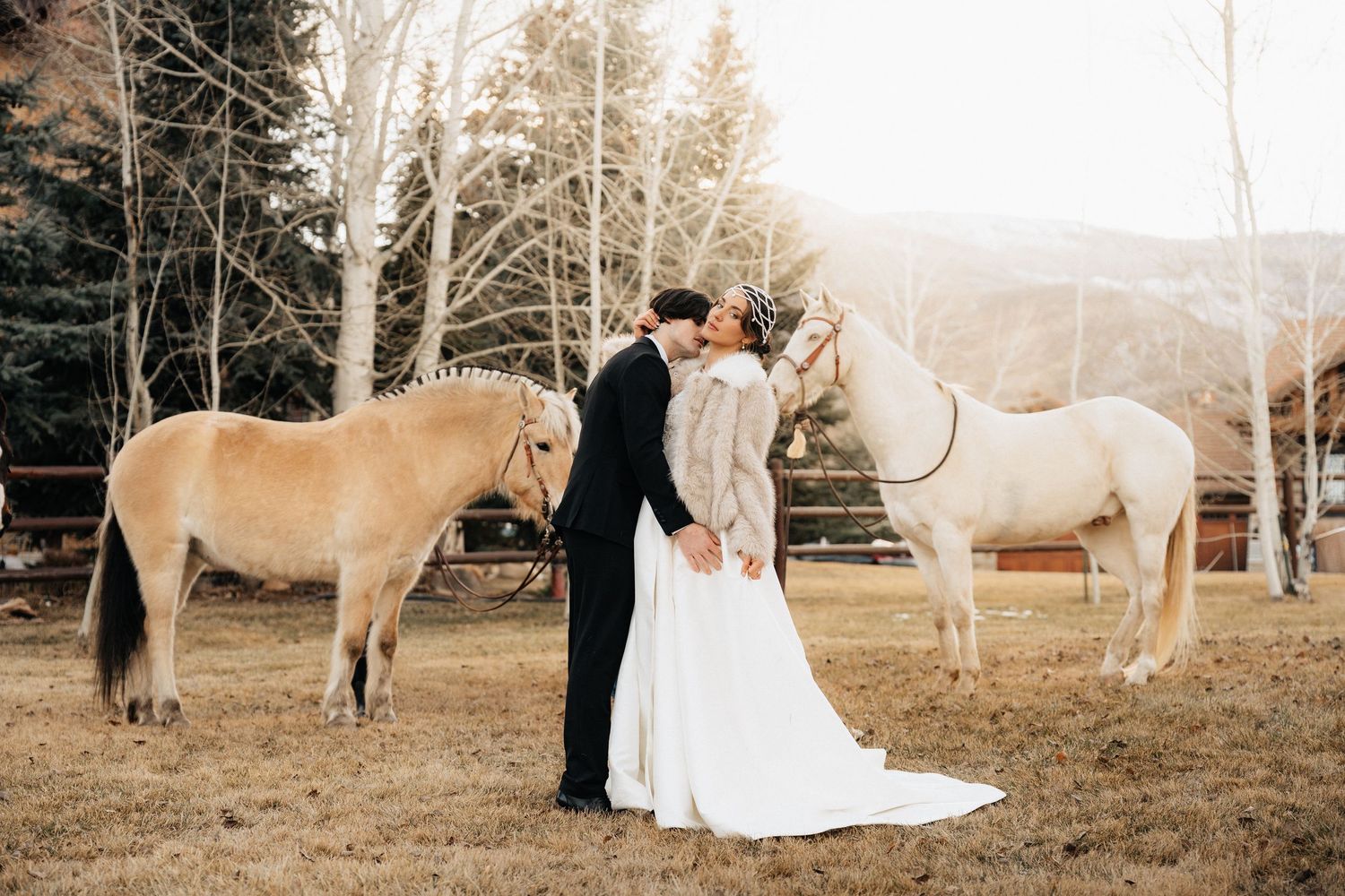 Couple poses with white horses during a rustic winter wedding photoshoot in Utah.