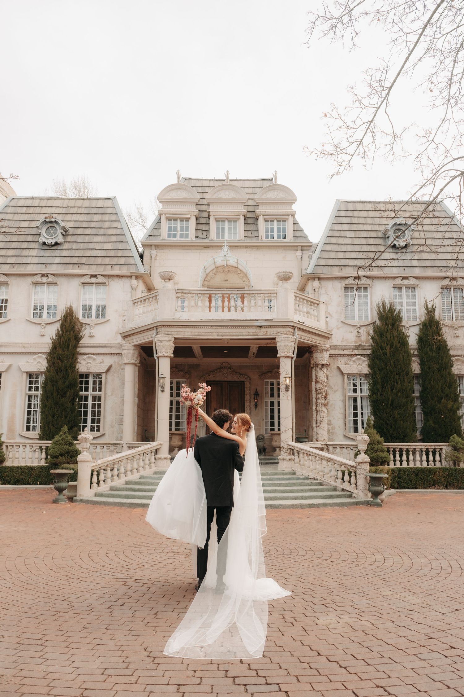 Romantic wedding lift pose in front of grand mansion with brick courtyard.