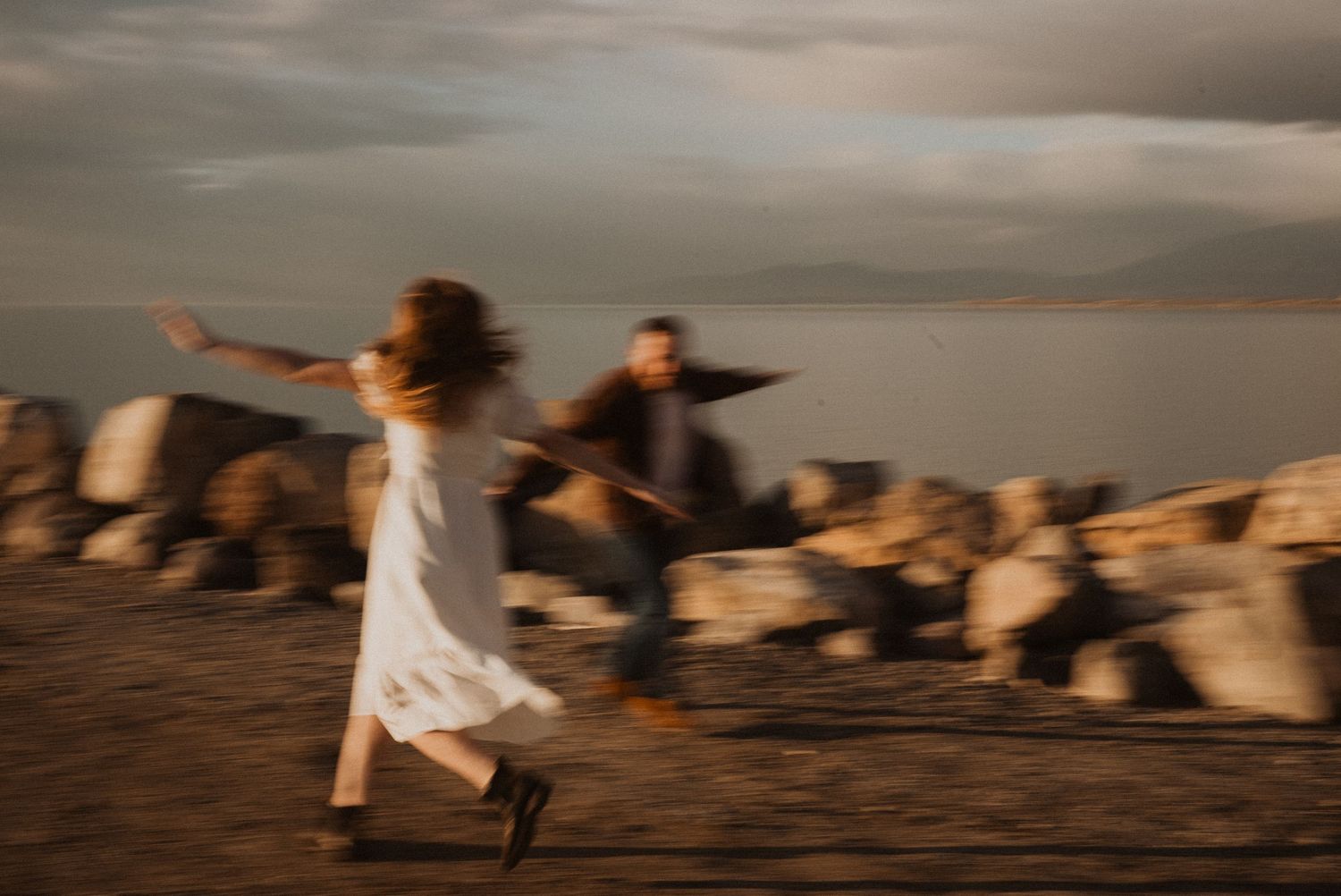 Motion-blurred couple runs joyfully along rocky coastline at sunset in Utah.