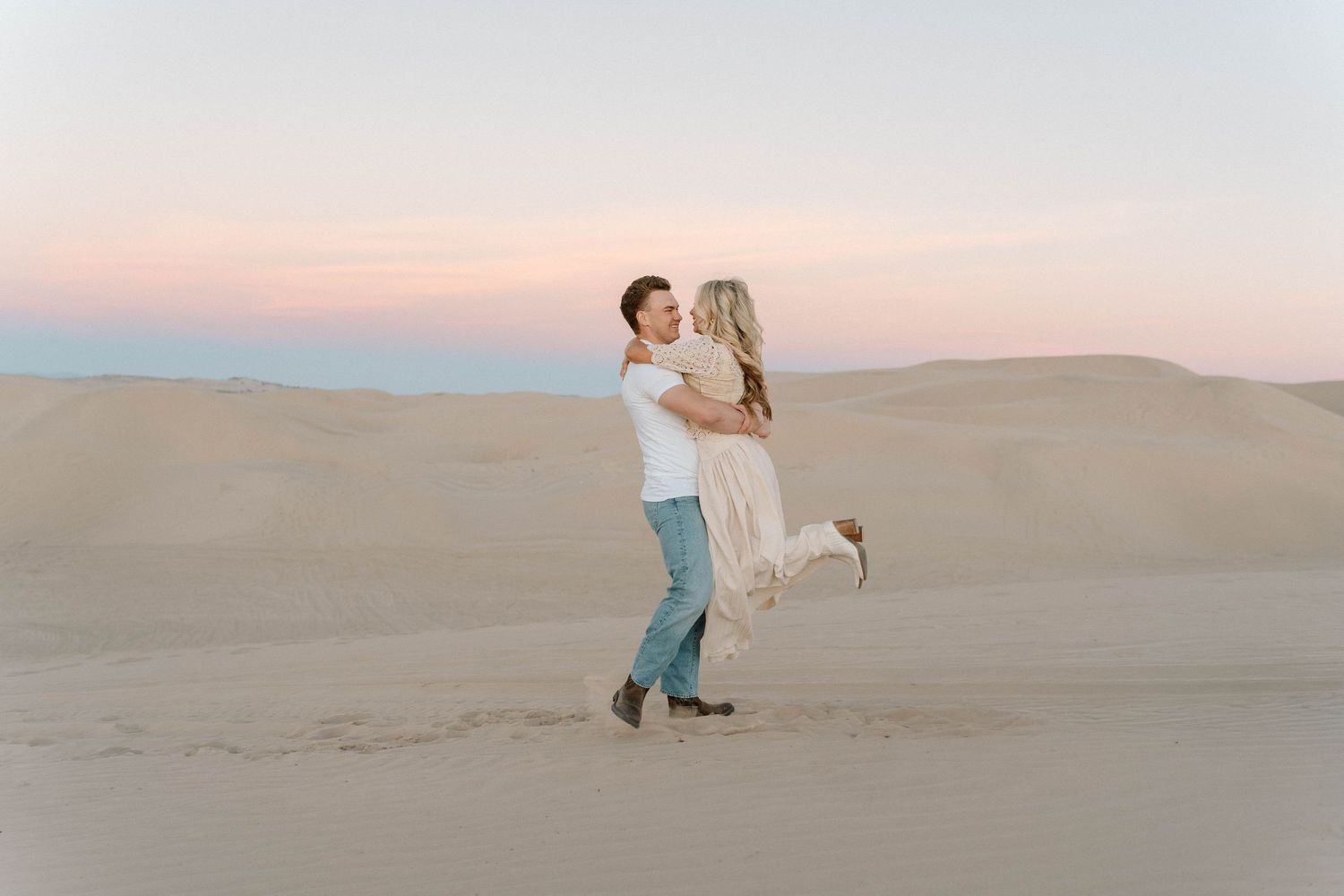 A couple shares a romantic moment together in a vast desert landscape during golden hour sunset.