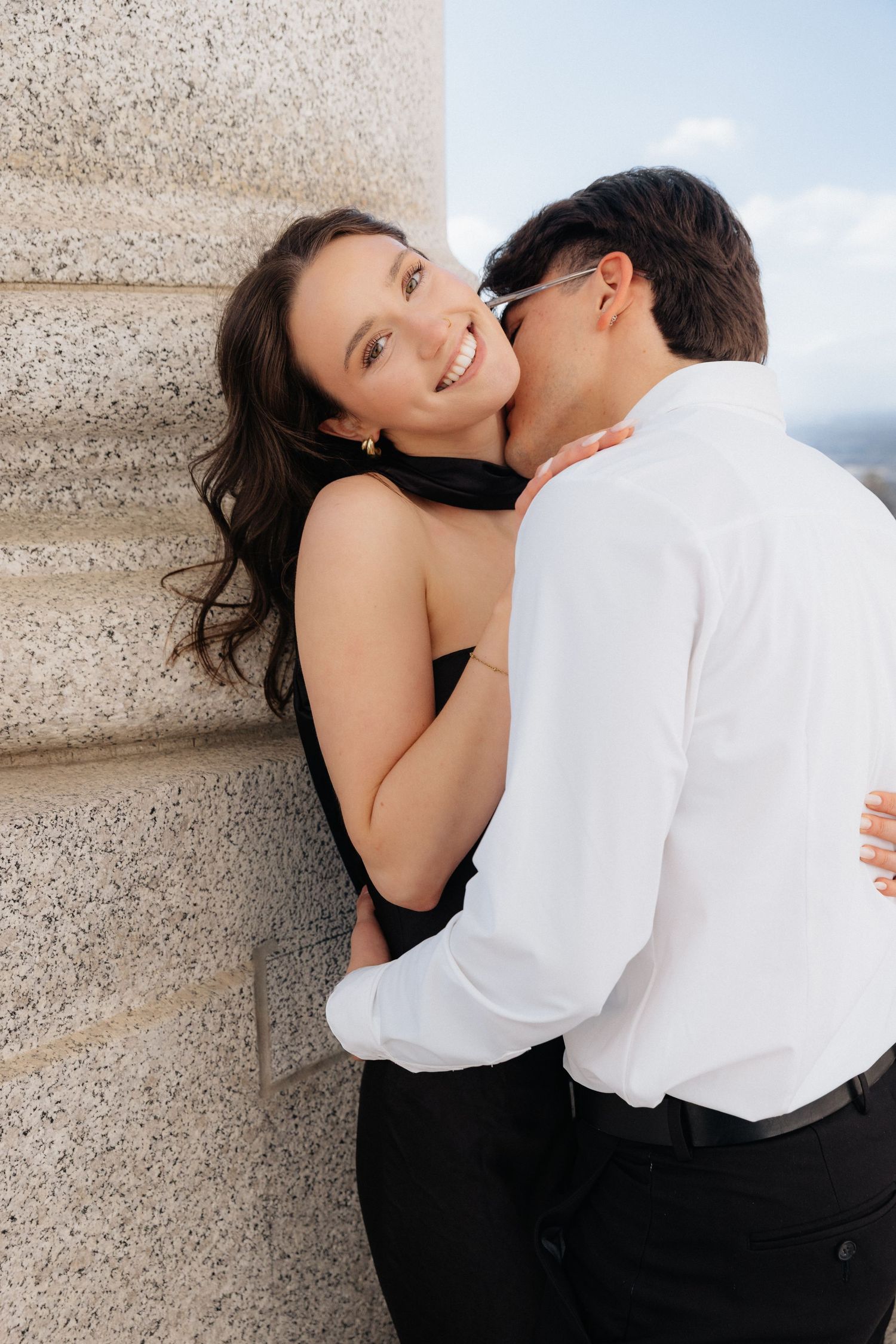 A romantic couple in black and white outfits embrace against a textured wall in a series of intimate engagement photos SLC capitol building