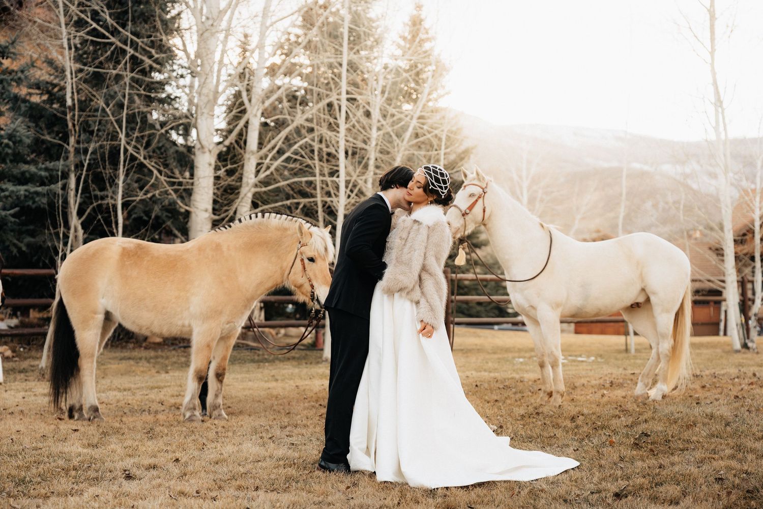 Wedding couple poses with two horses in a snowy winter setting in Utah.