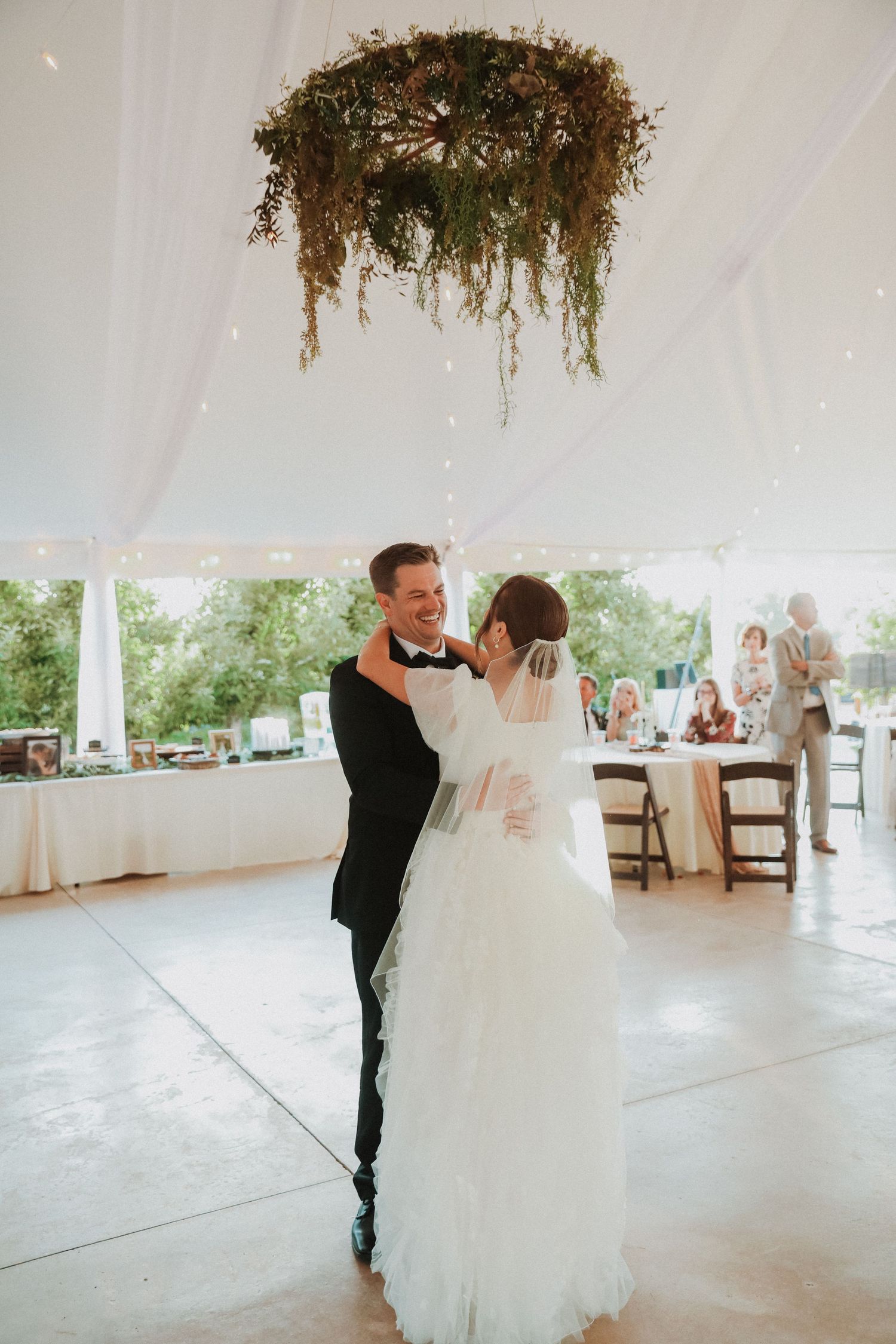 Wedding couple shares first dance under hanging floral installation in white tent reception.