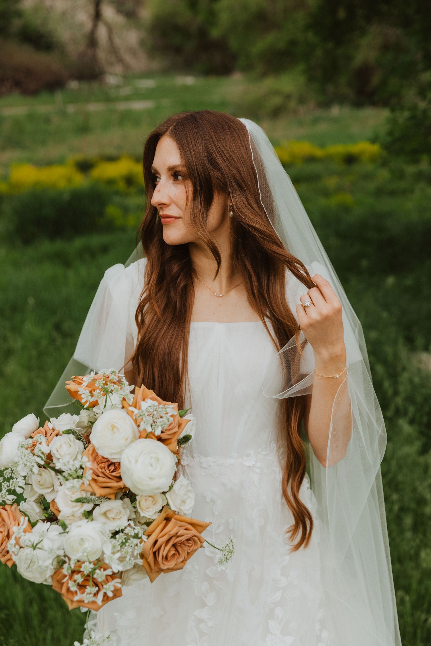 Bridal portrait showcasing a delicate white gown and peachy floral bouquet in natural outdoor setting.