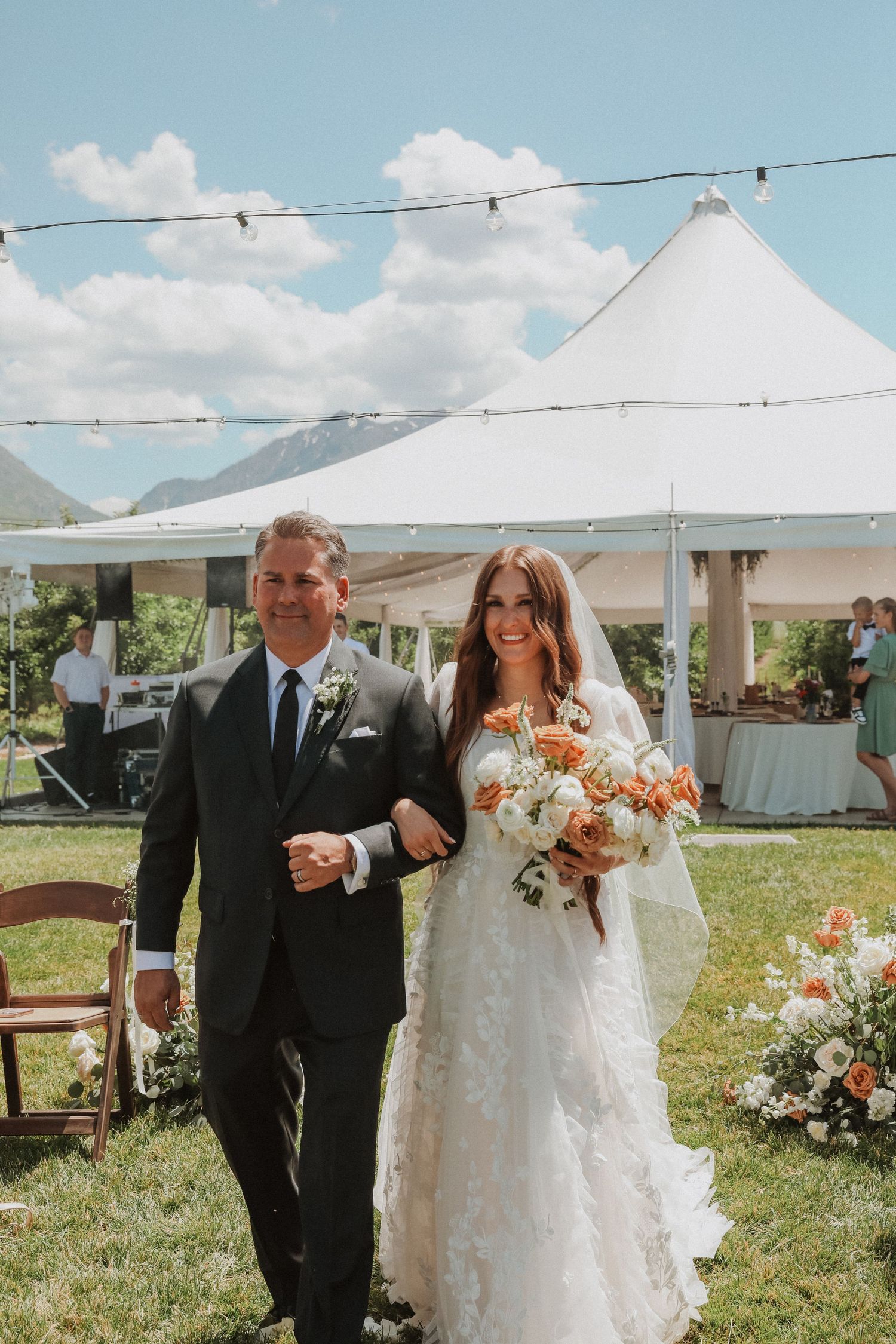 Outdoor wedding ceremony under white tents with floral arrangements and wooden chairs.
