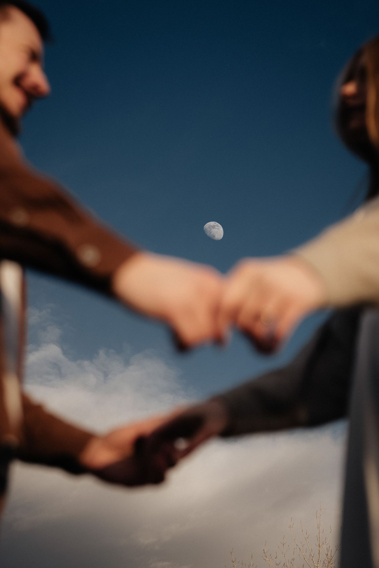 Silhouetted hands reaching toward each other against a deep blue sky with visible moon.
