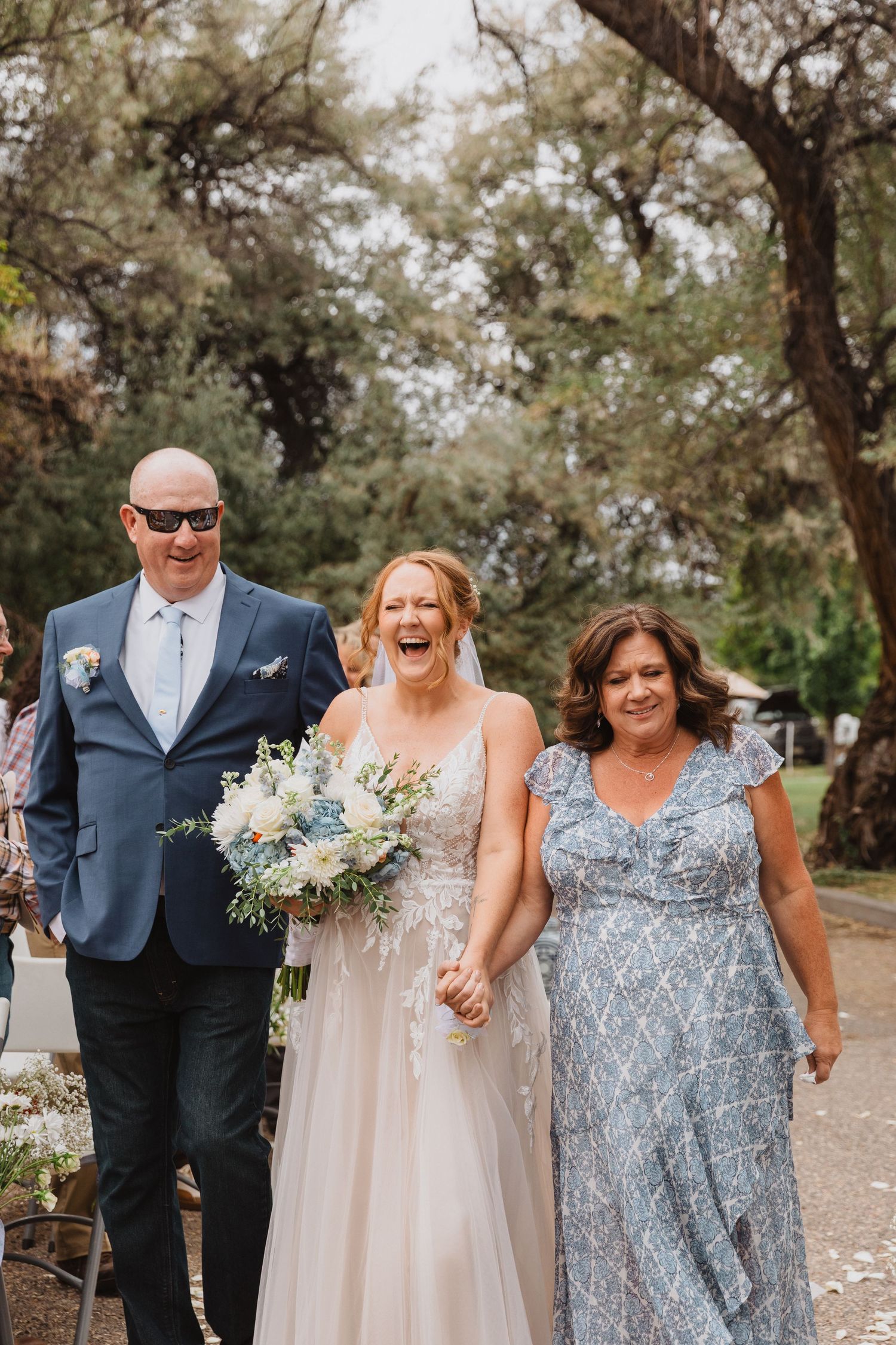 Wedding party members laugh and celebrate outdoors in blue and neutral attire.