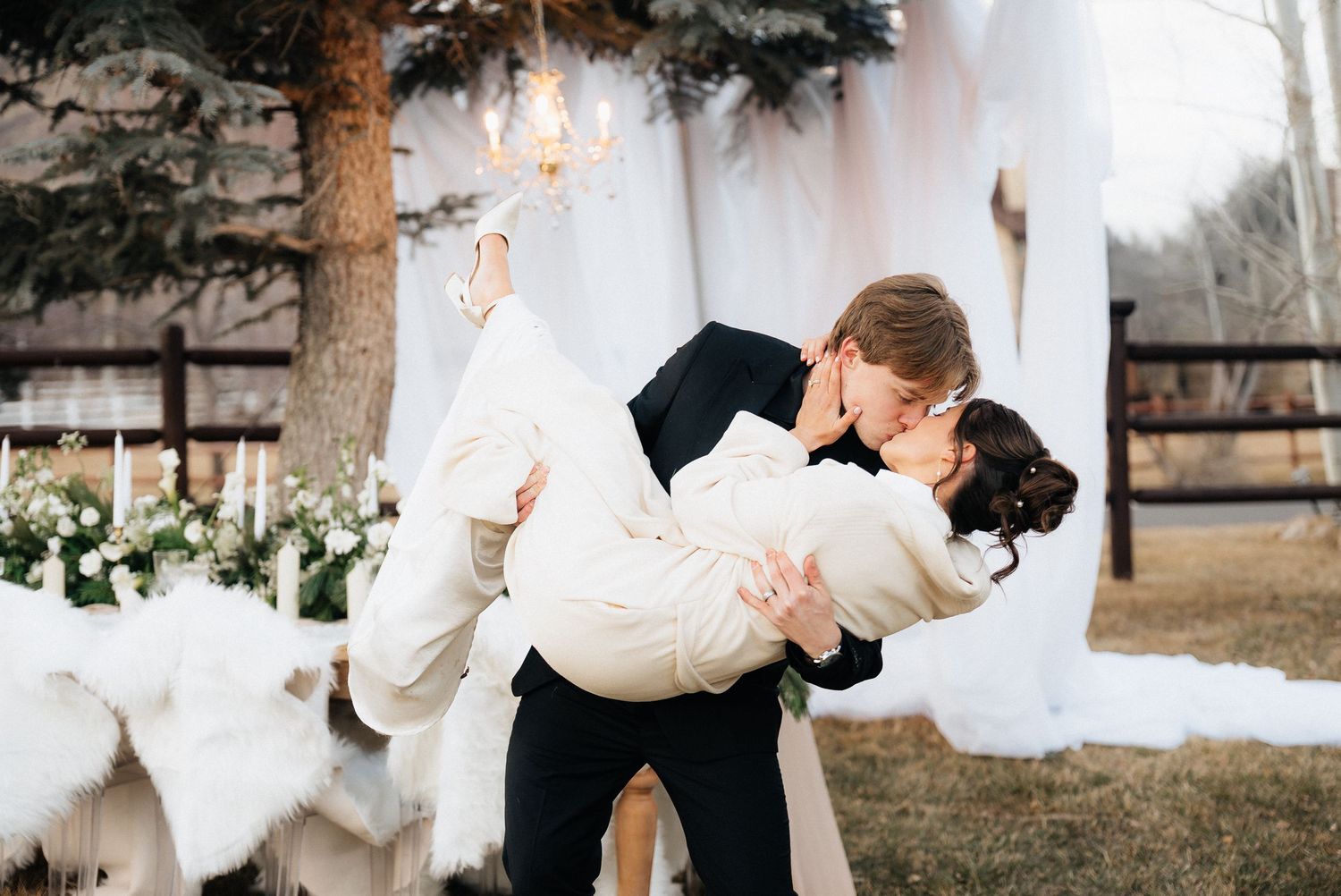 Romantic wedding couple embraces in front of white draped fabric and evergreen trees in Utah.