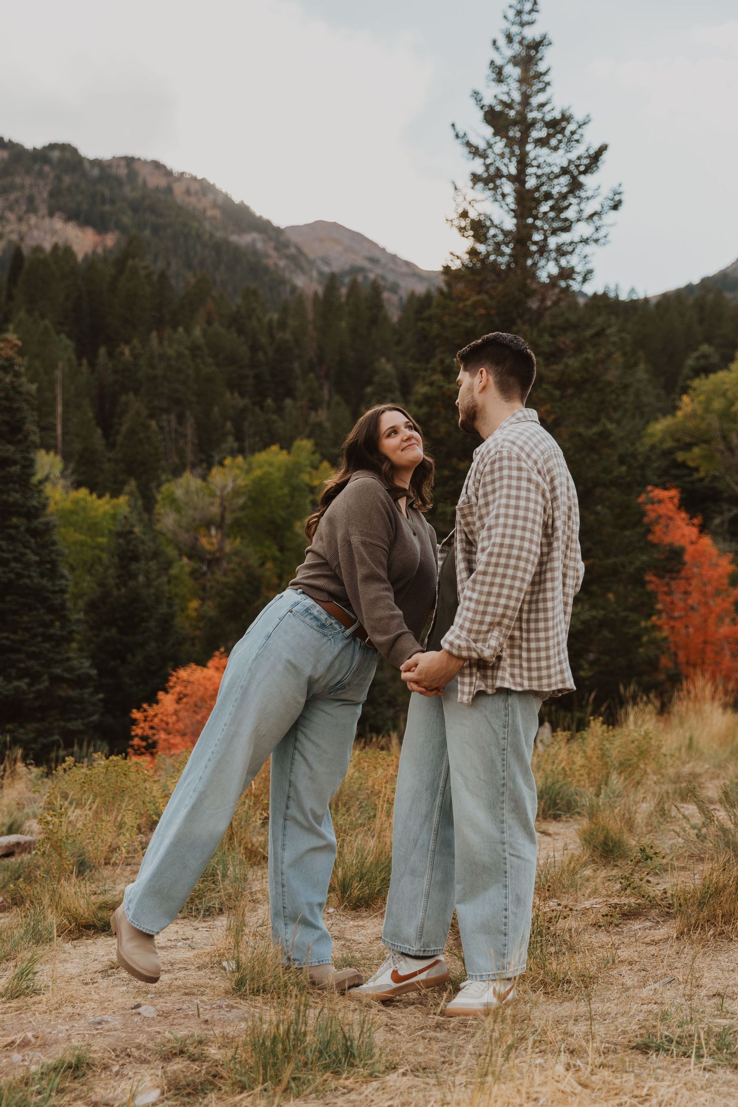 A couple playfully poses together against a backdrop of autumn mountains and evergreen trees Tibble Fork Utah County.