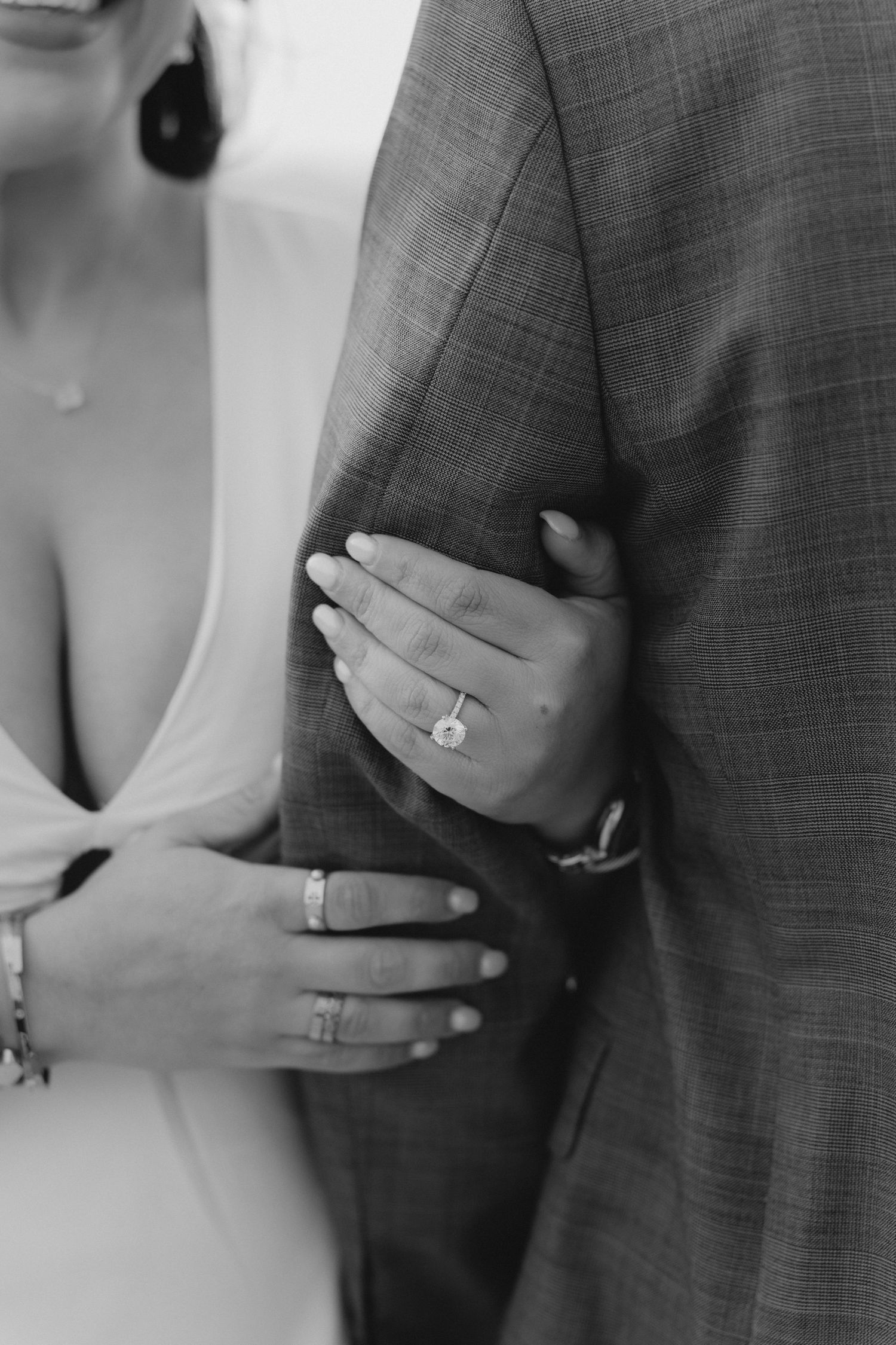 Black and white photo of bride and groom arms linked, showcasing elegant engagement ring and wedding bands.