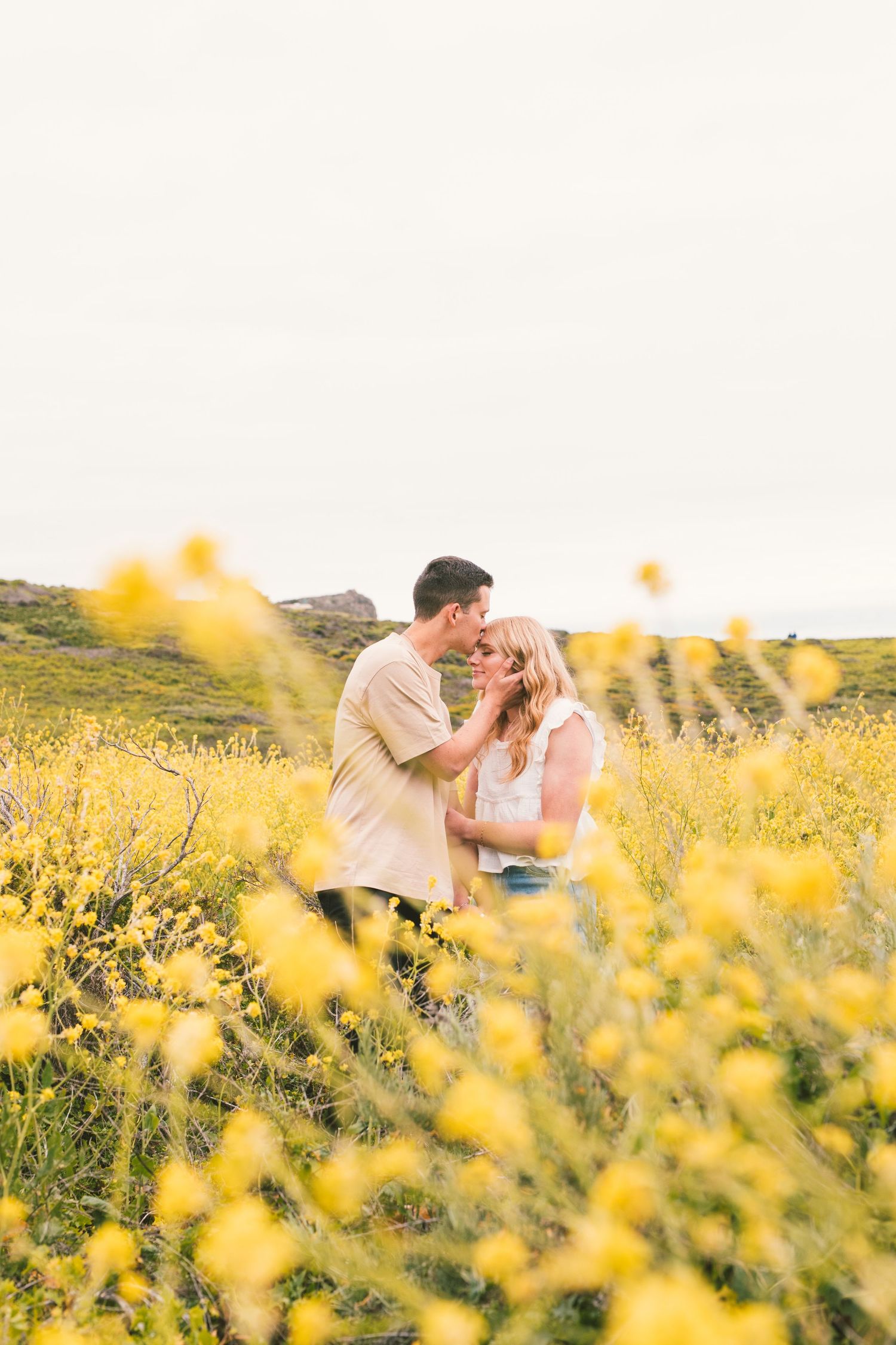 Romantic couple sharing intimate moments in field of bright yellow wildflowers at sunset.