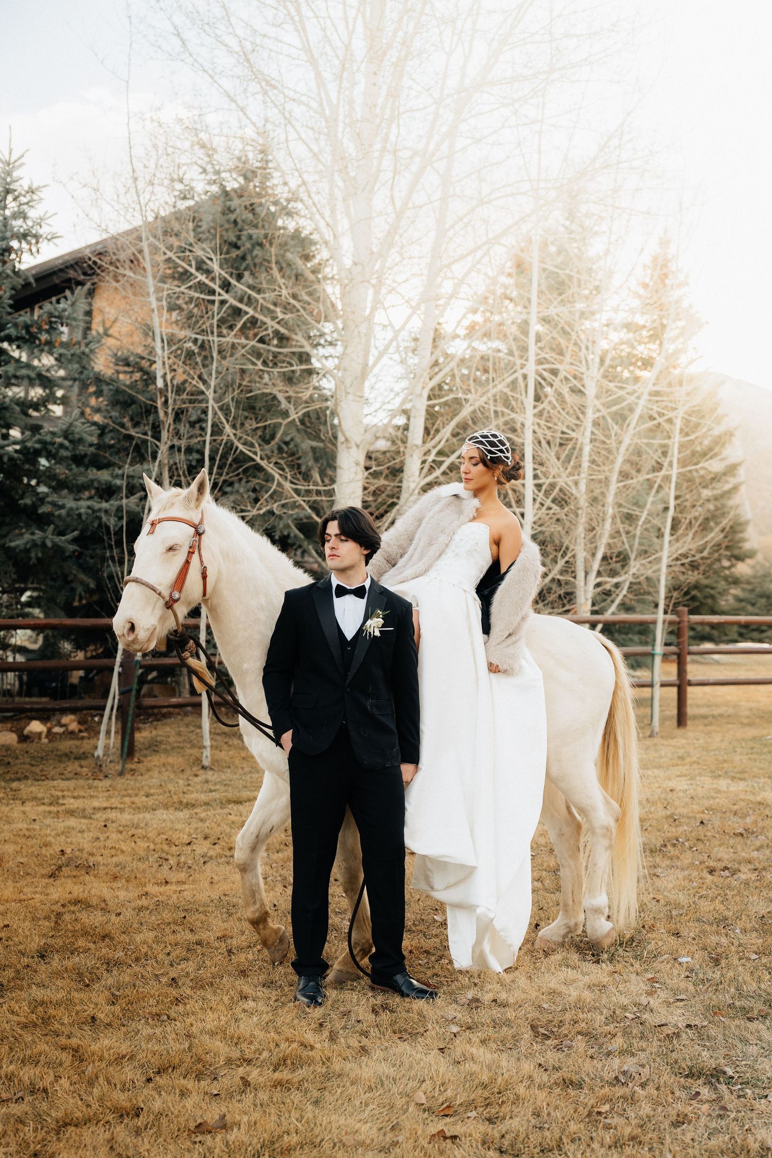 A couple poses with a white horse in a rustic outdoor setting during a winter wedding photoshoot in Utah.