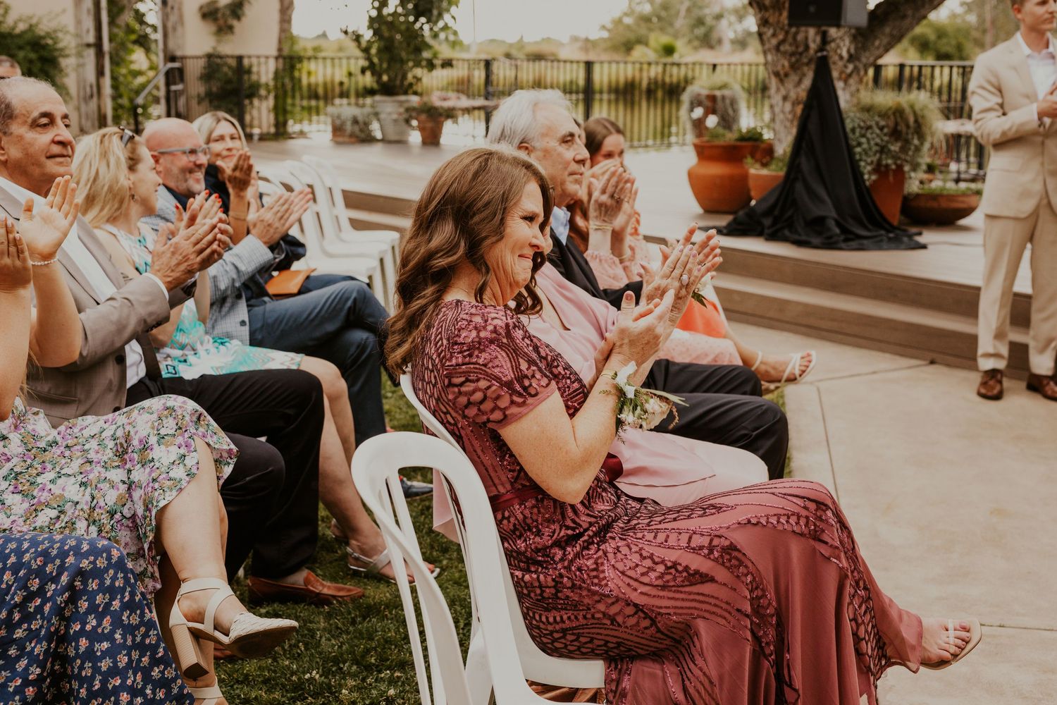 Wedding guests seated in white chairs during outdoor ceremony.
