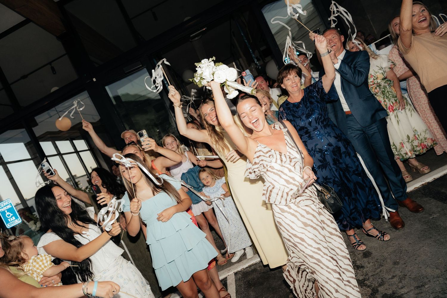 Bride tosses bouquet to excited guests at lively wedding reception celebration indoors.
