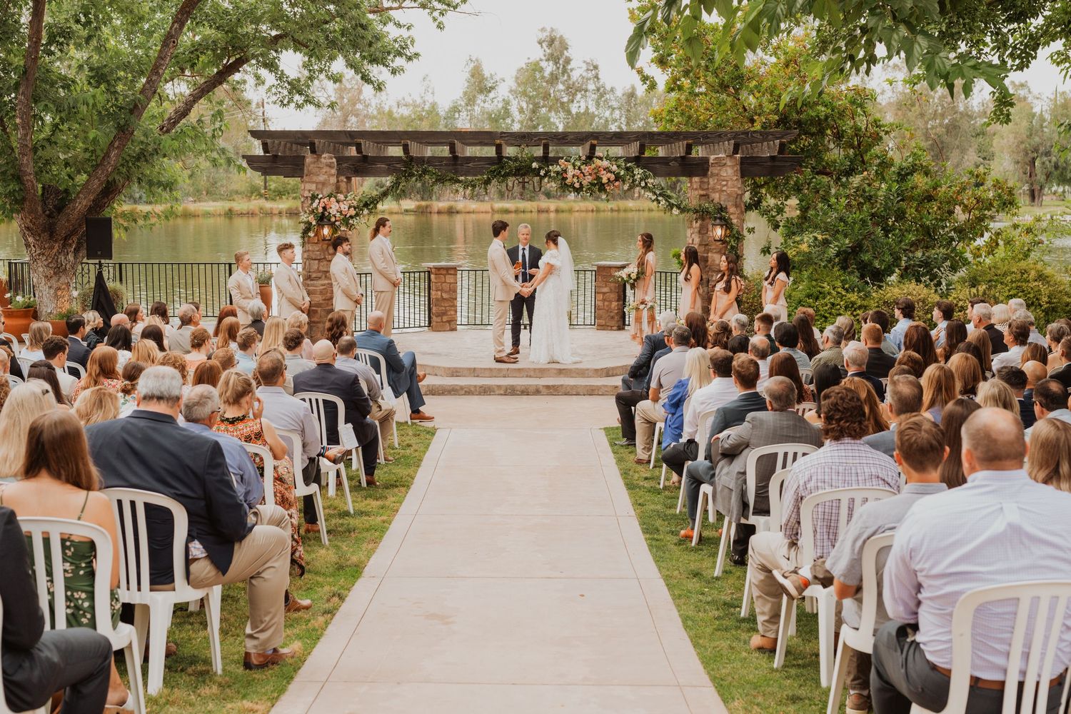 Outdoor wedding ceremony setup with white chairs and natural landscaping.