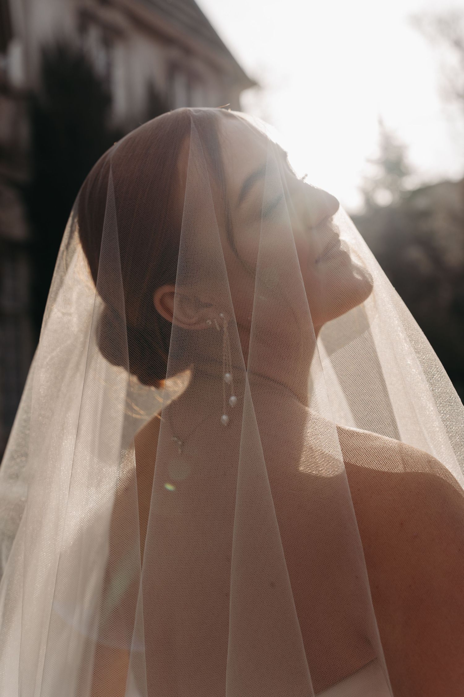 Ethereal bridal portrait through delicate veil with dramatic backlighting.