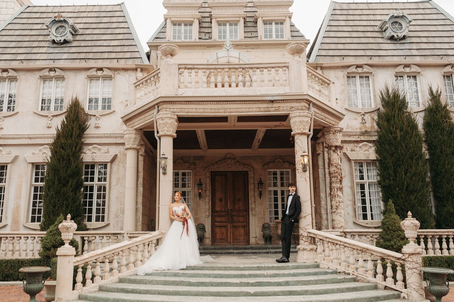 Panoramic view of a luxurious stone mansion with symmetrical architecture and manicured cypress trees.
