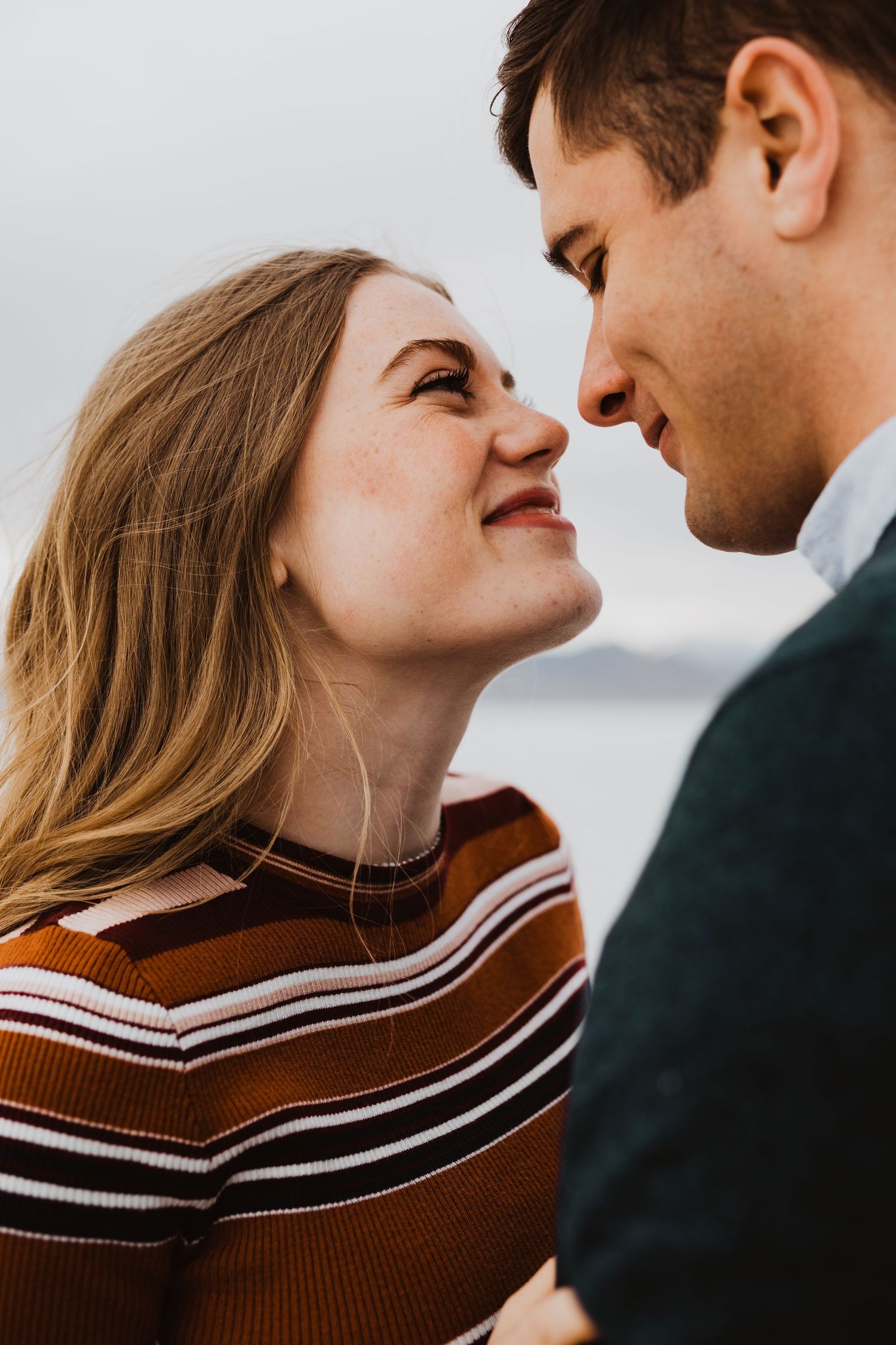 Close-up romantic portrait series showing couple in brown striped sweater against light background.