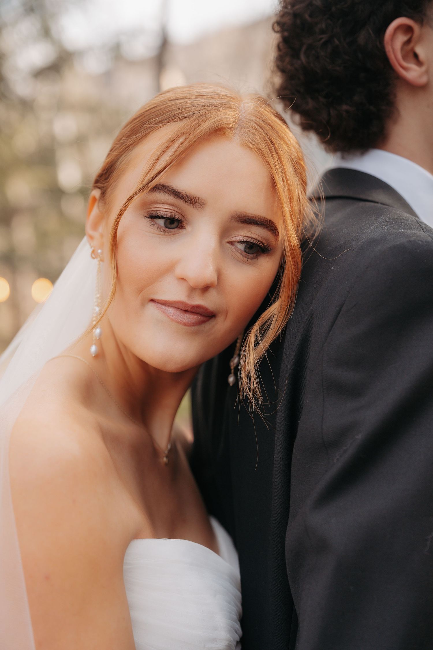 Romantic wedding couple in white dress and black suit share intimate close-up moments in a garden setting.