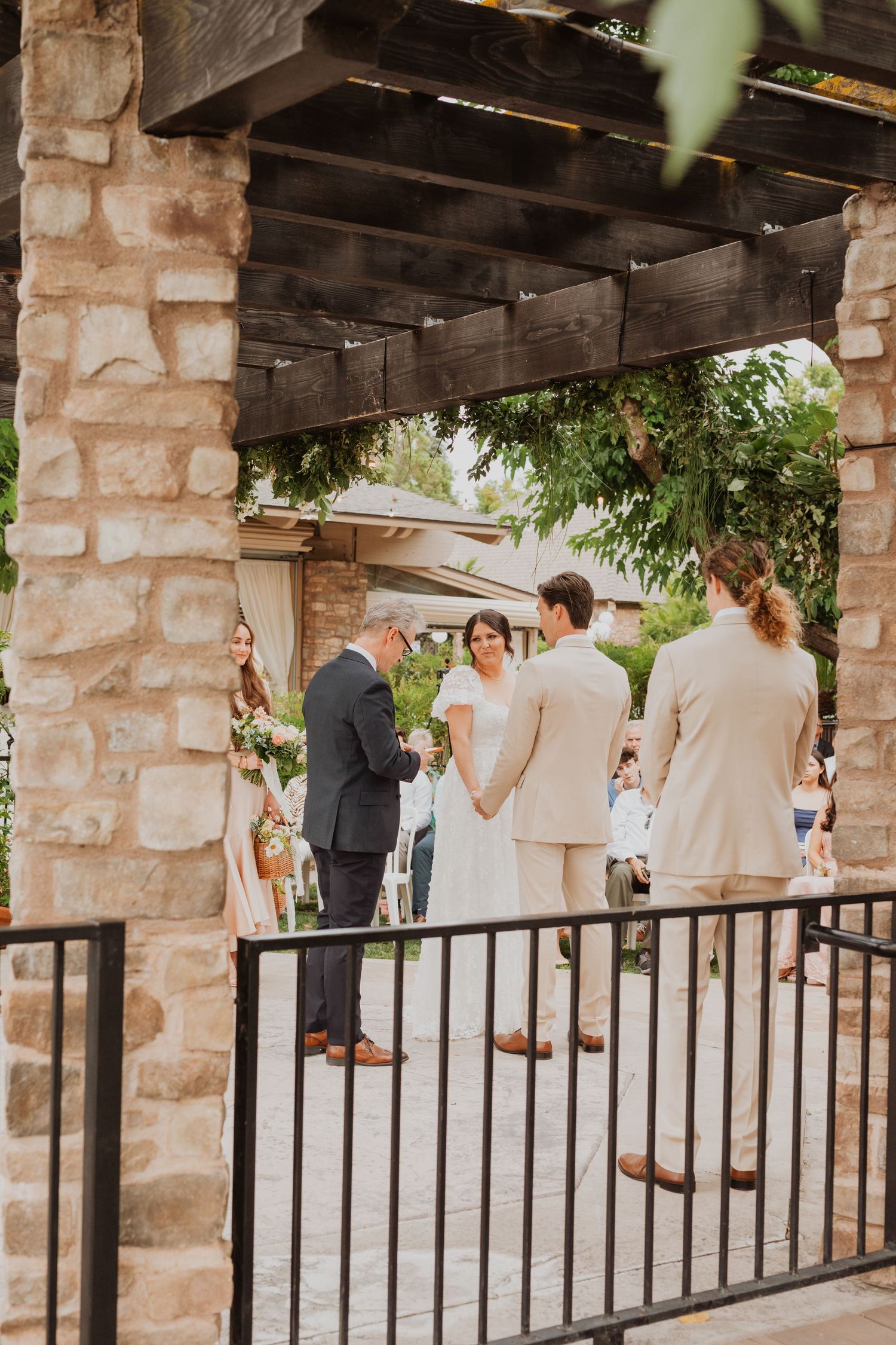 Wedding party gathered under rustic stone pergola with black metal railings.
