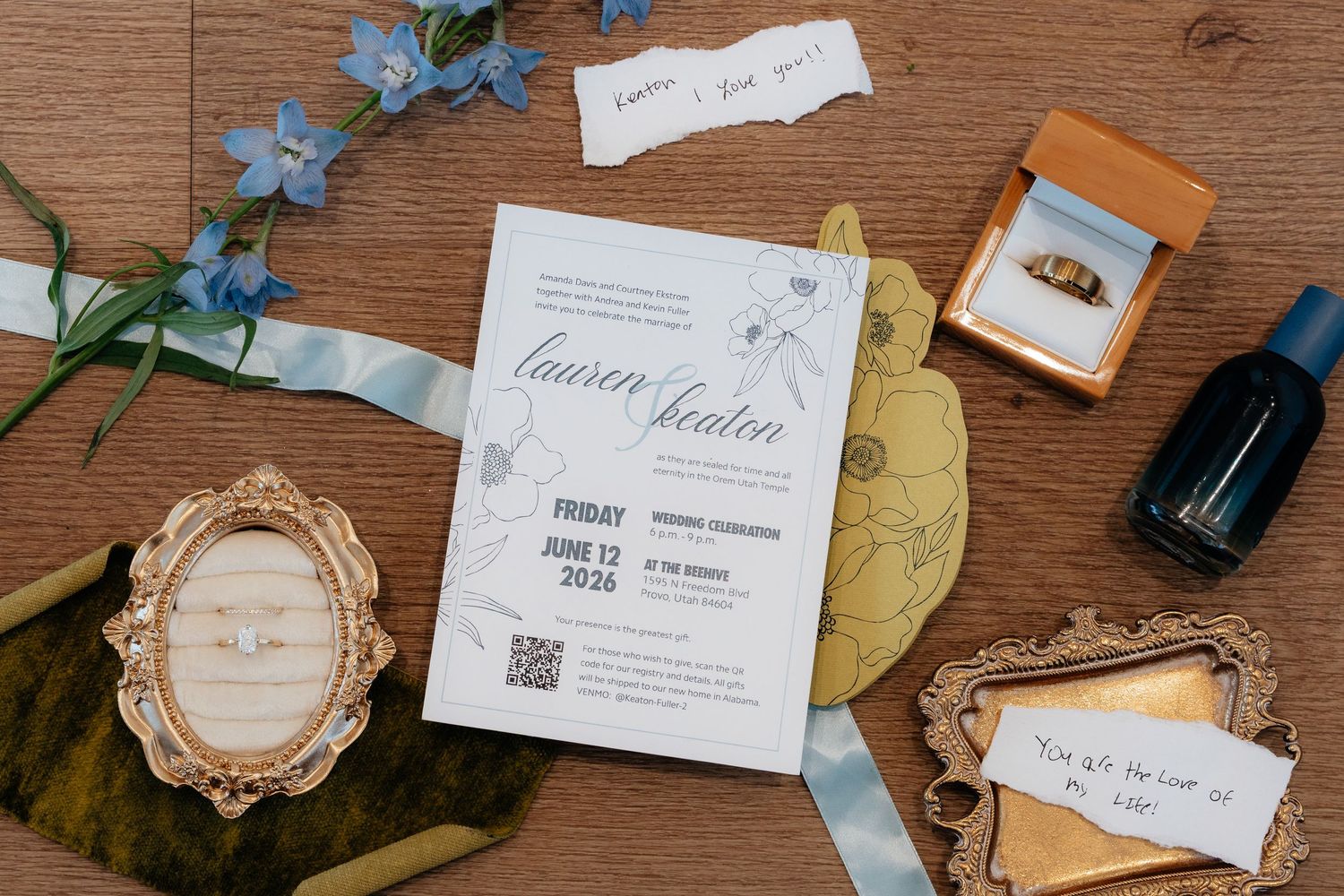 Wedding invitation suite for Lauren and Keaton on June 13, 2026, with blue florals, gold frames, and ring box on wood.