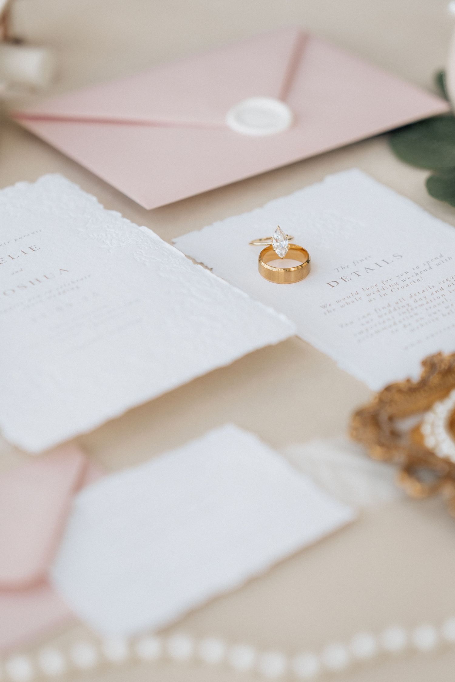 Wedding stationery with pearl necklace, gold ring, and eucalyptus leaves on light pink background.