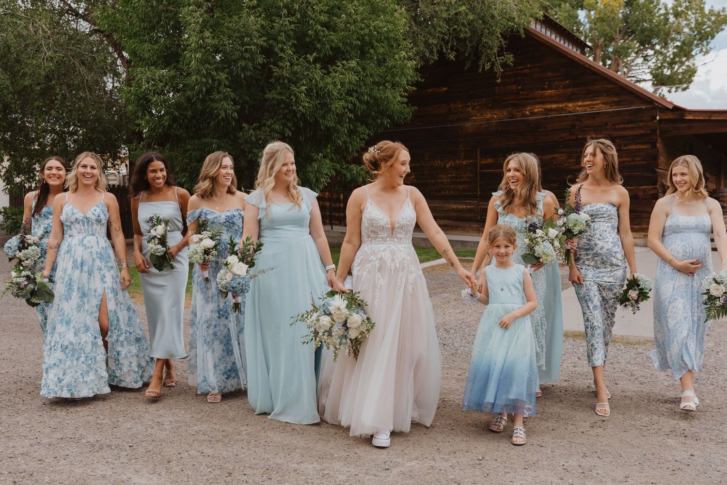 Bridal party walks together outdoors in coordinated blue and neutral attire.