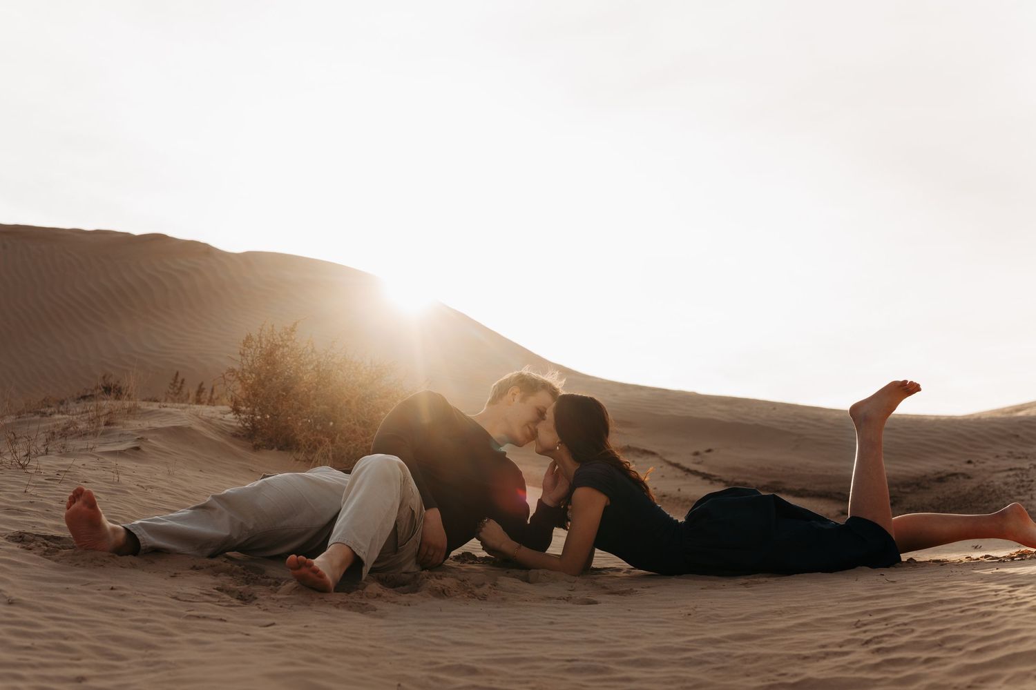 A person lies peacefully on desert sand dunes during golden hour as sunlight creates a warm, ethereal glow.
