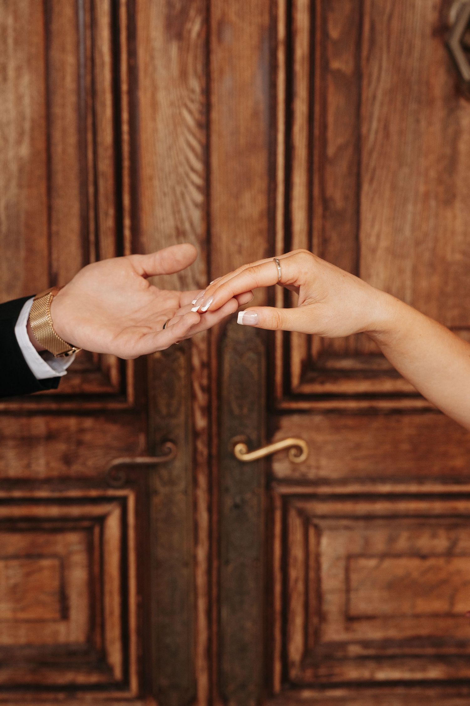 Two hands reaching towards each other against a backdrop of ornate wooden doors in a dramatic lighting setup.