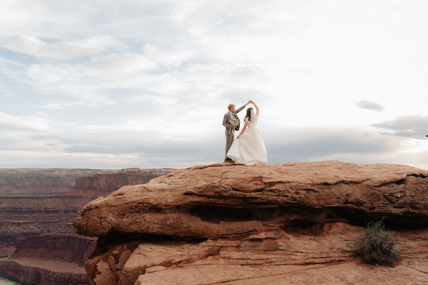 Bride and groom dancing on red rock canyon cliff edge at sunset in Moab Utah wedding photo.