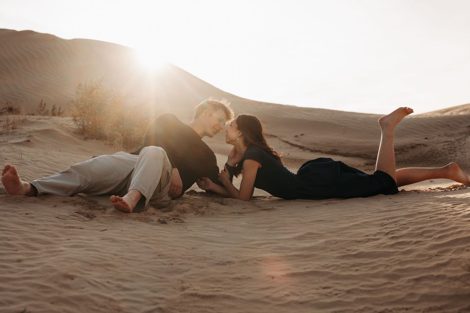 Couple relaxing together on sandy beach at sunset with warm golden light and silhouettes.