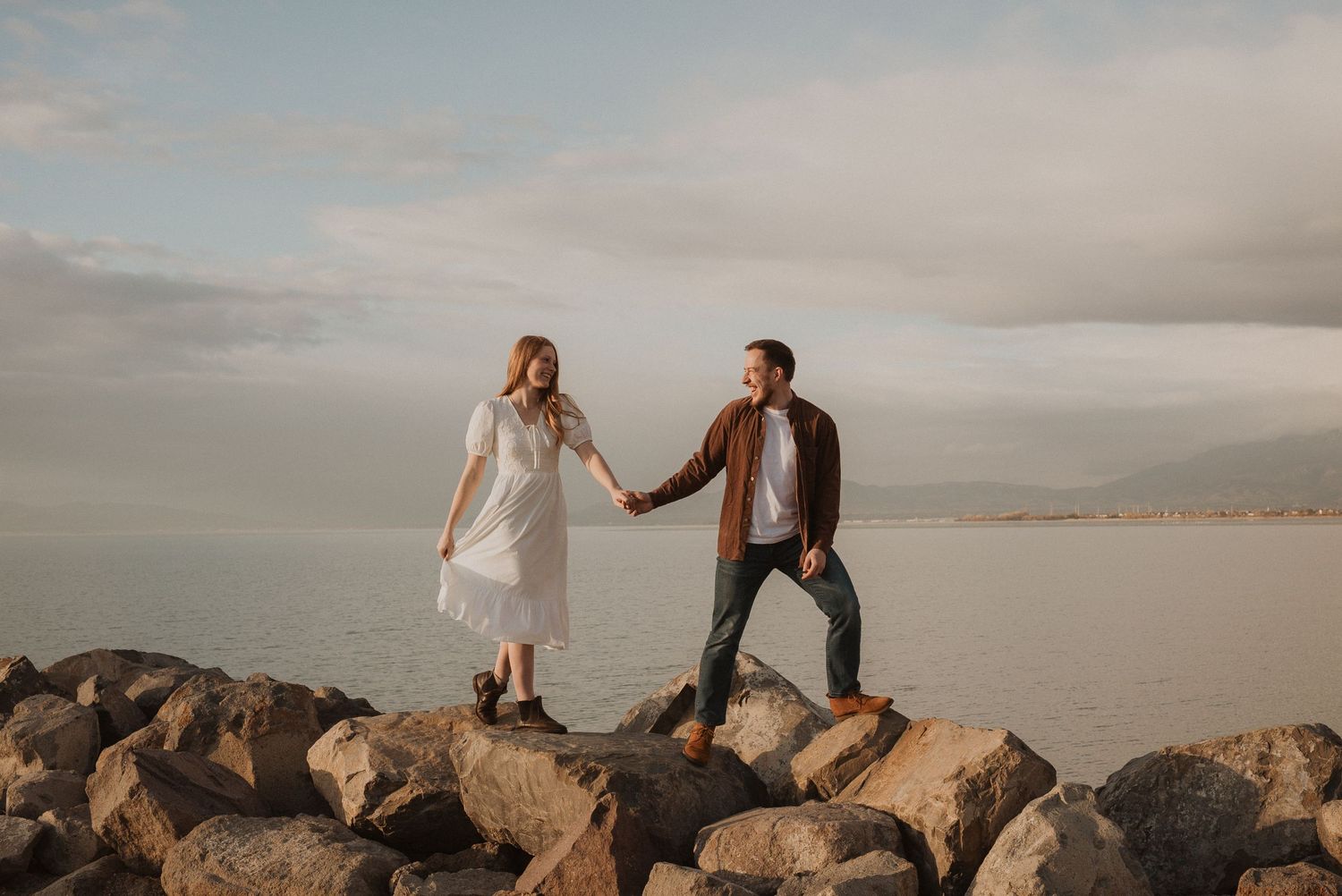 Couple shares intimate moment on rocky beach during sunset photoshoot.