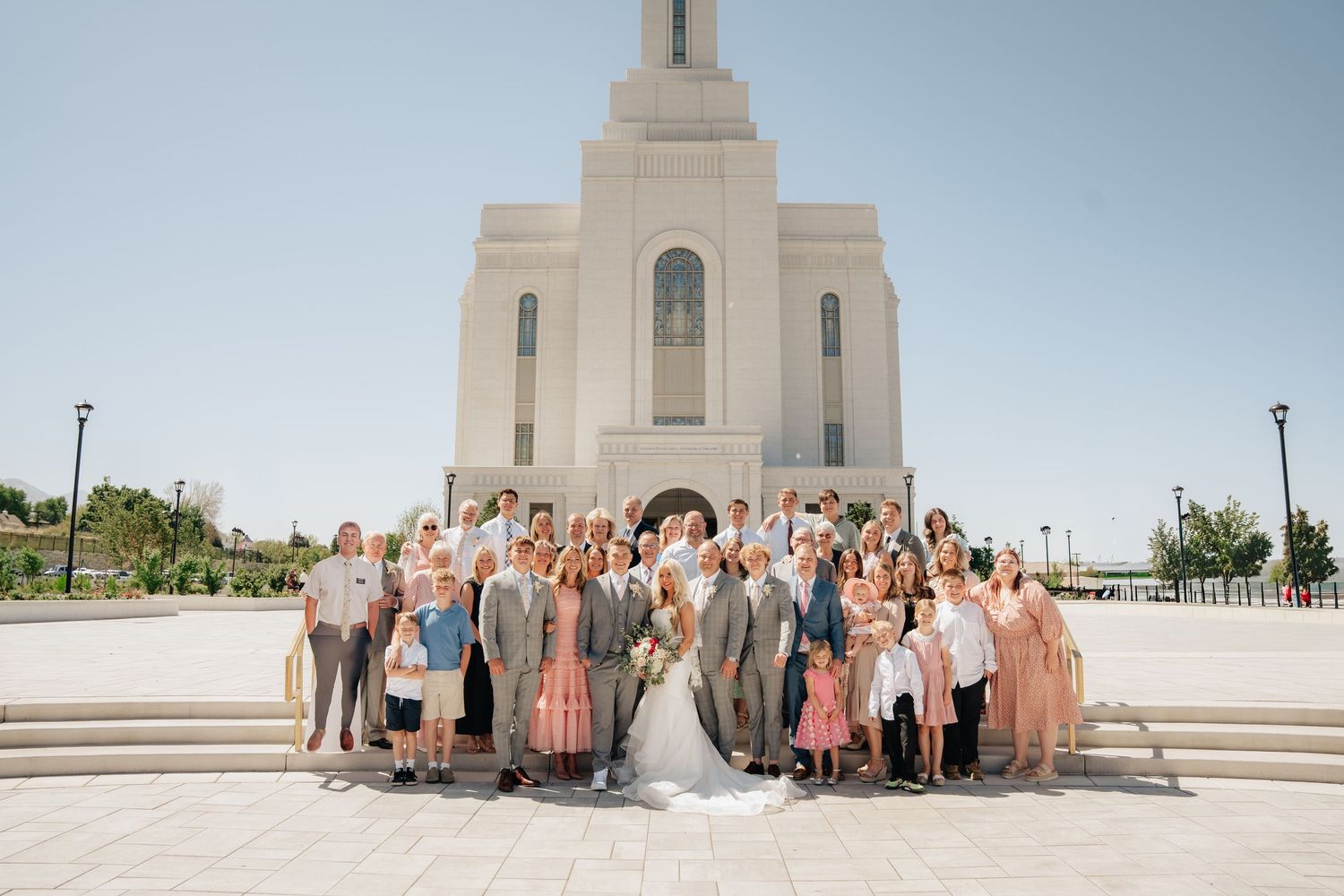 Large wedding party poses on steps outside a grand LDS temple on a sunny day.