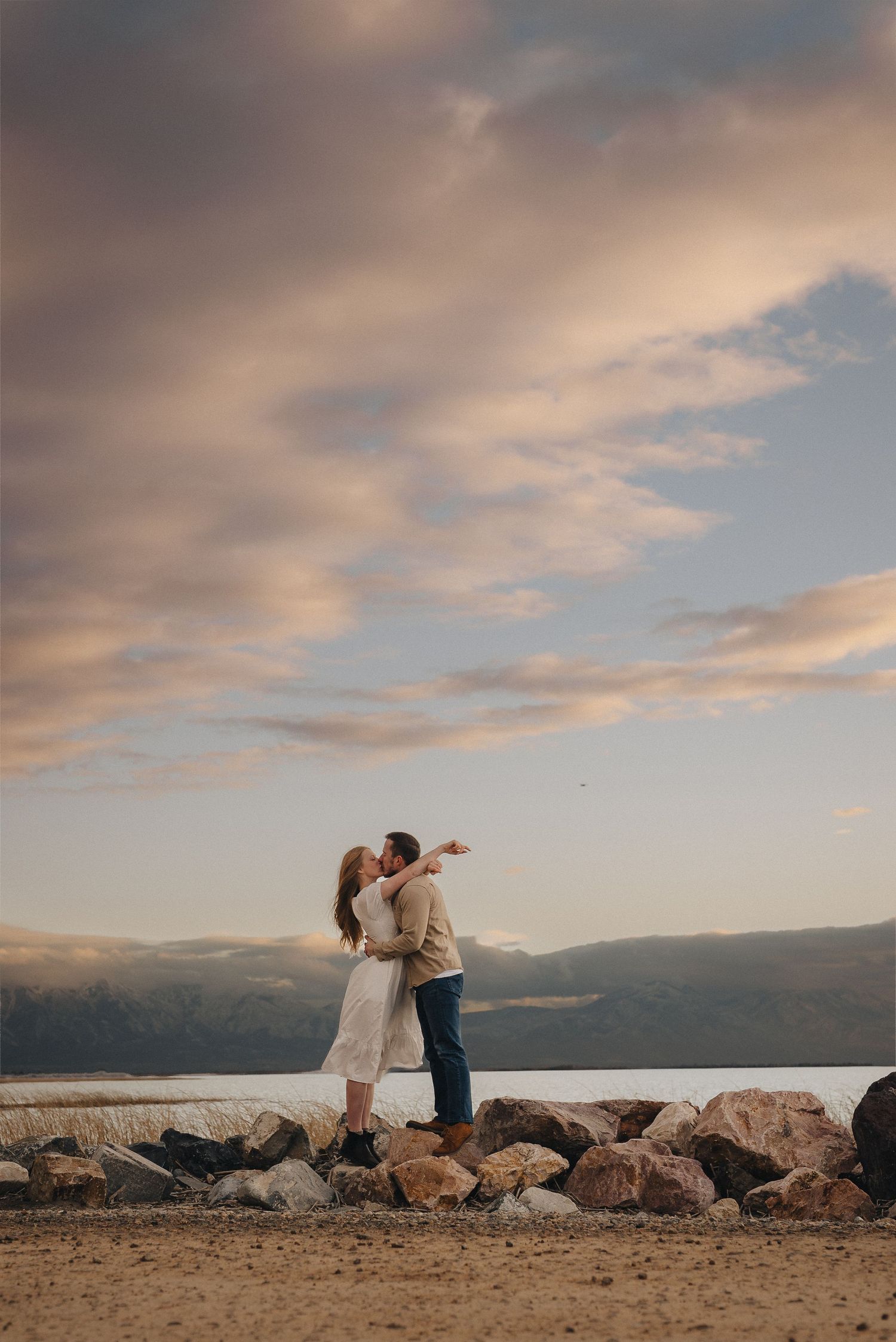Romantic sunset photoshoot on rocky beach with mountains in background.