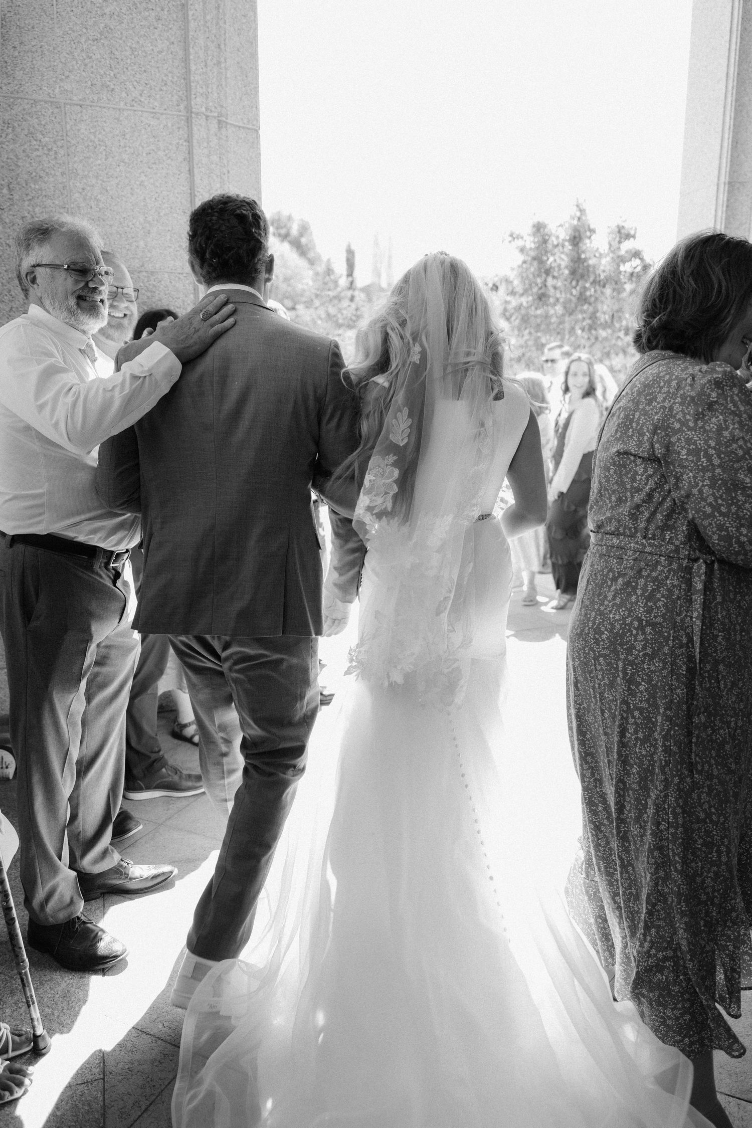 Black and white photo of bride and groom walking out of wedding venue surrounded by guests.