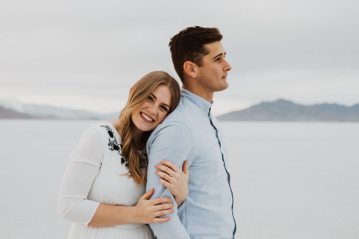 Playful couple laughing and hugging on salt flats with mountains visible in distance.
